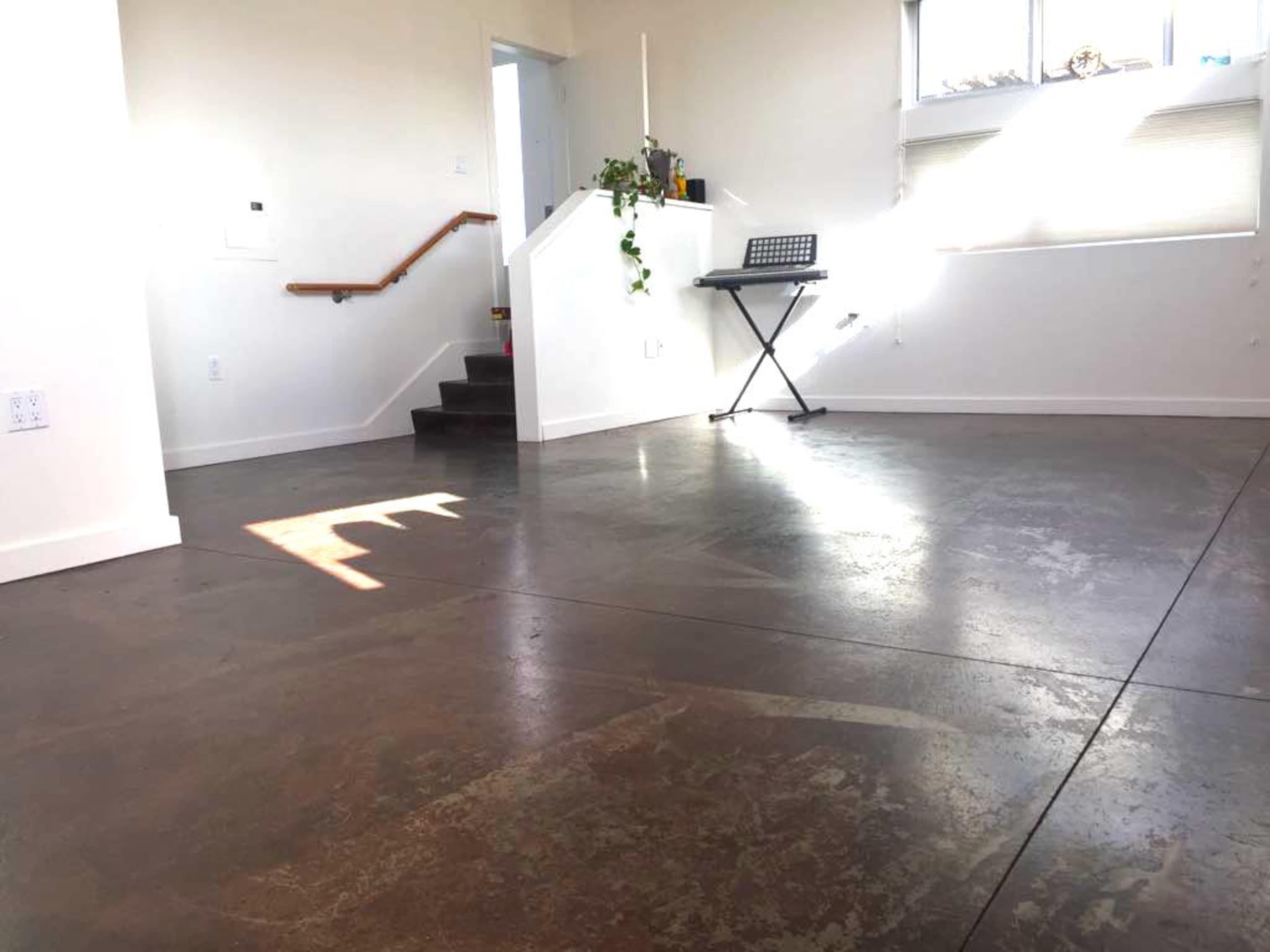 A spacious room with polished concrete flooring, a set of stairs leading to an upper level, and a keyboard stand against the wall.