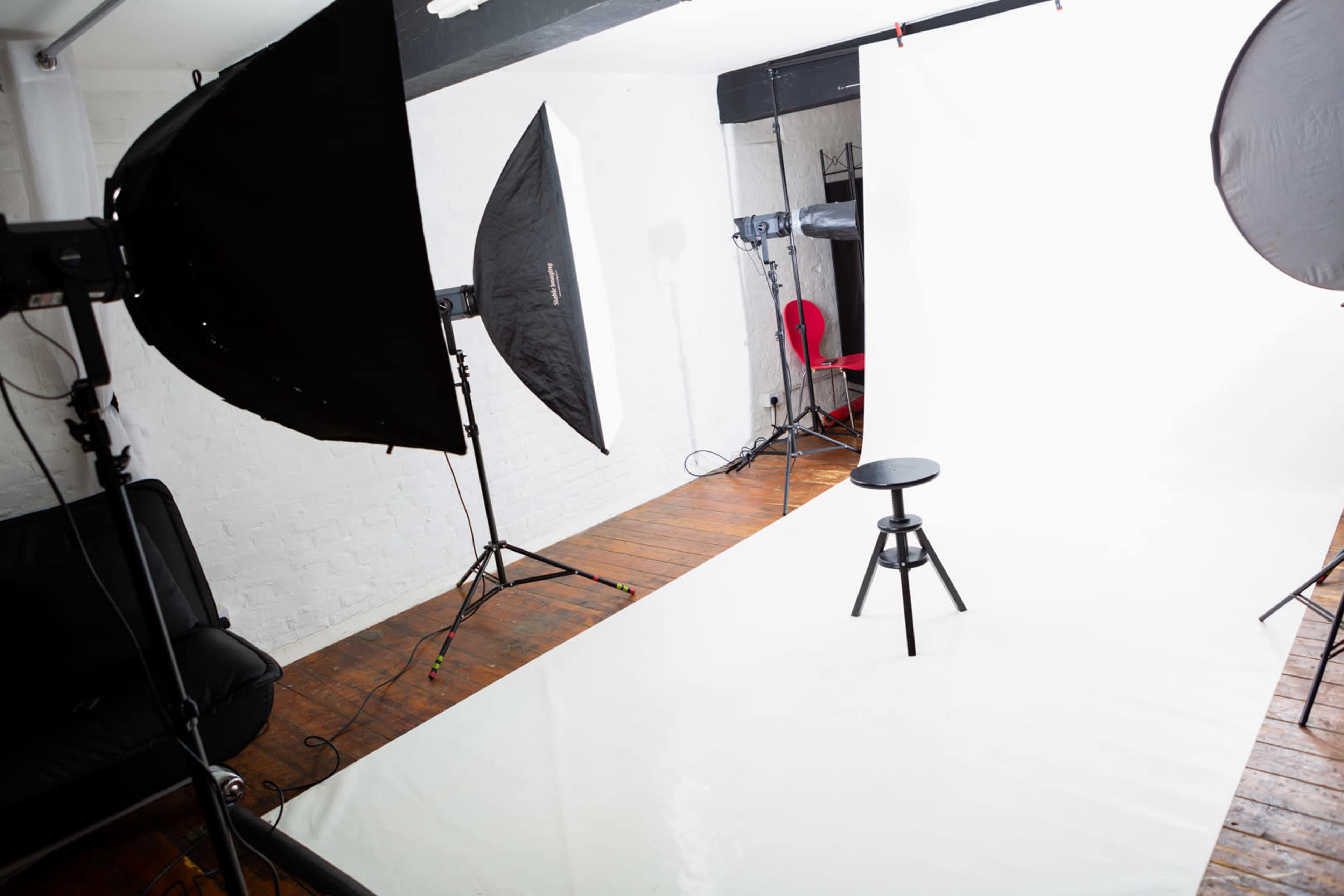 A photography studio with softbox lighting and a black stool positioned on a white backdrop.