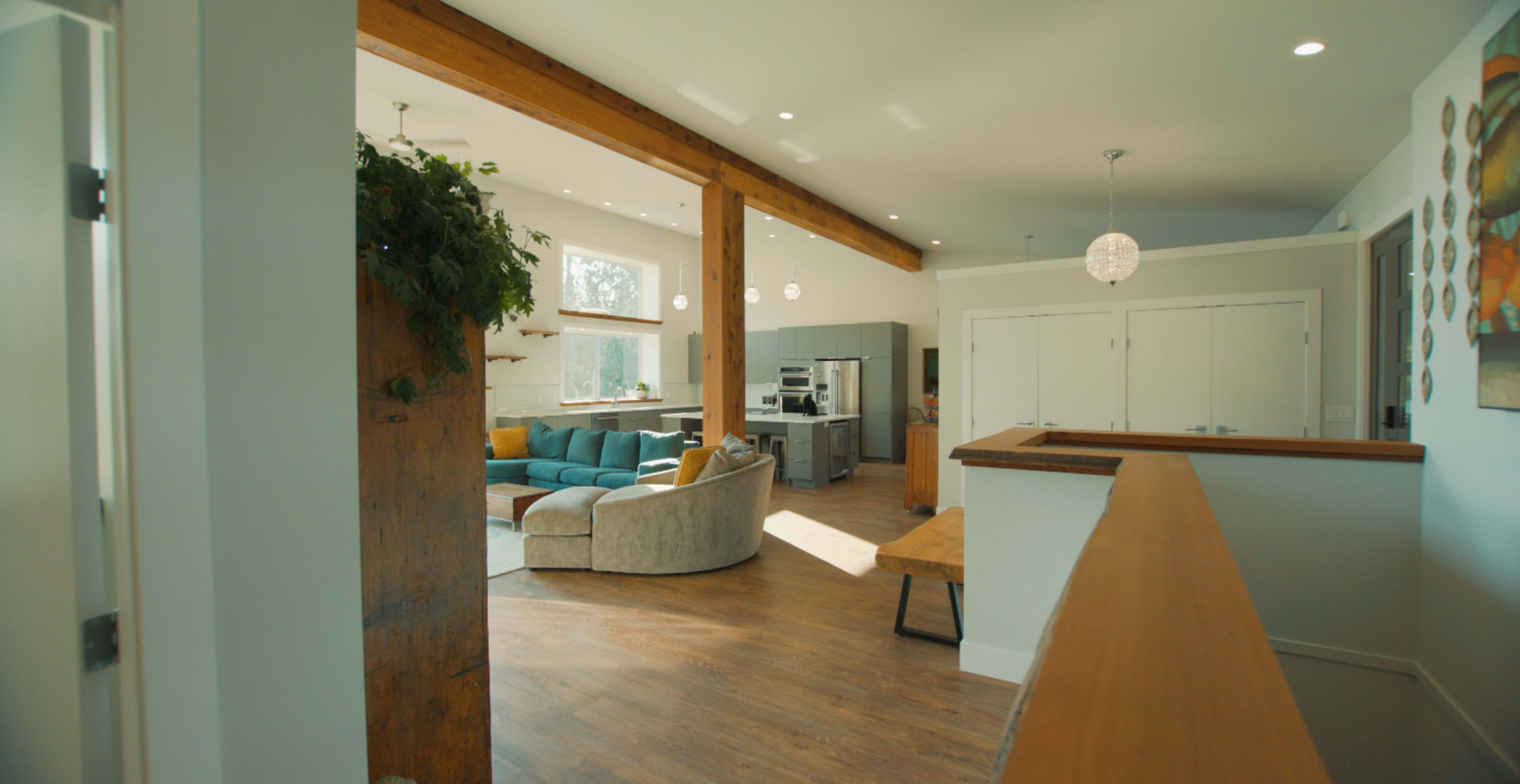 A modern interior space with a kitchen and living area, featuring wooden beams, large windows, and a blue sectional sofa.