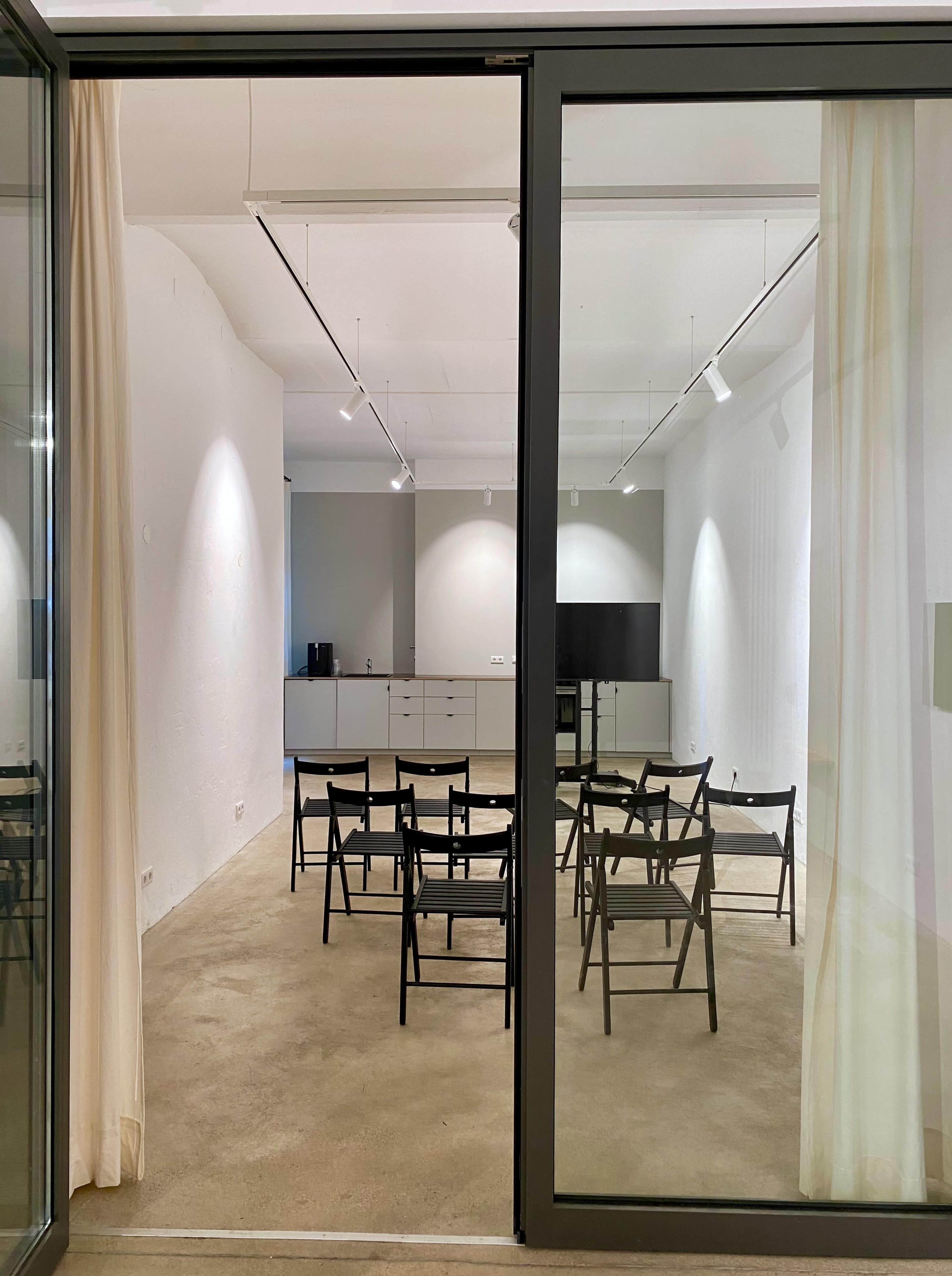 A minimalist meeting room with several black chairs arranged around a central space and a gray wall in the background.