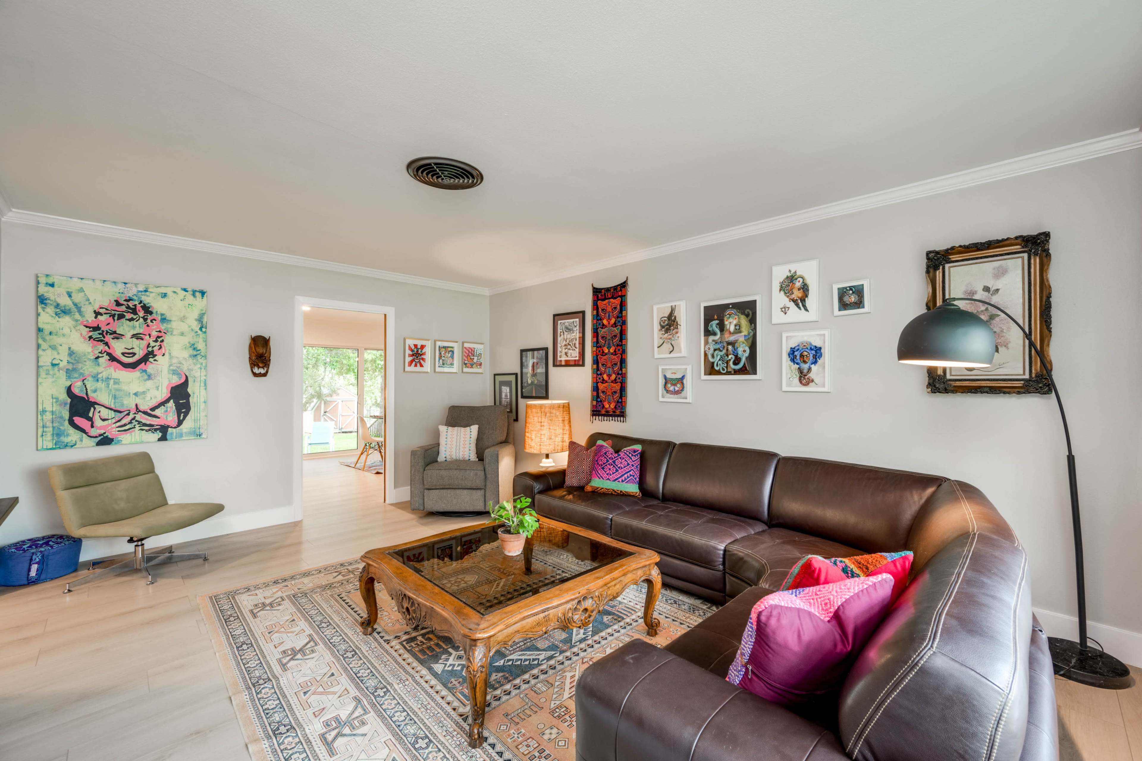 The image shows a living room featuring a brown leather sectional sofa, a wooden coffee table, and a variety of framed artwork on the walls.