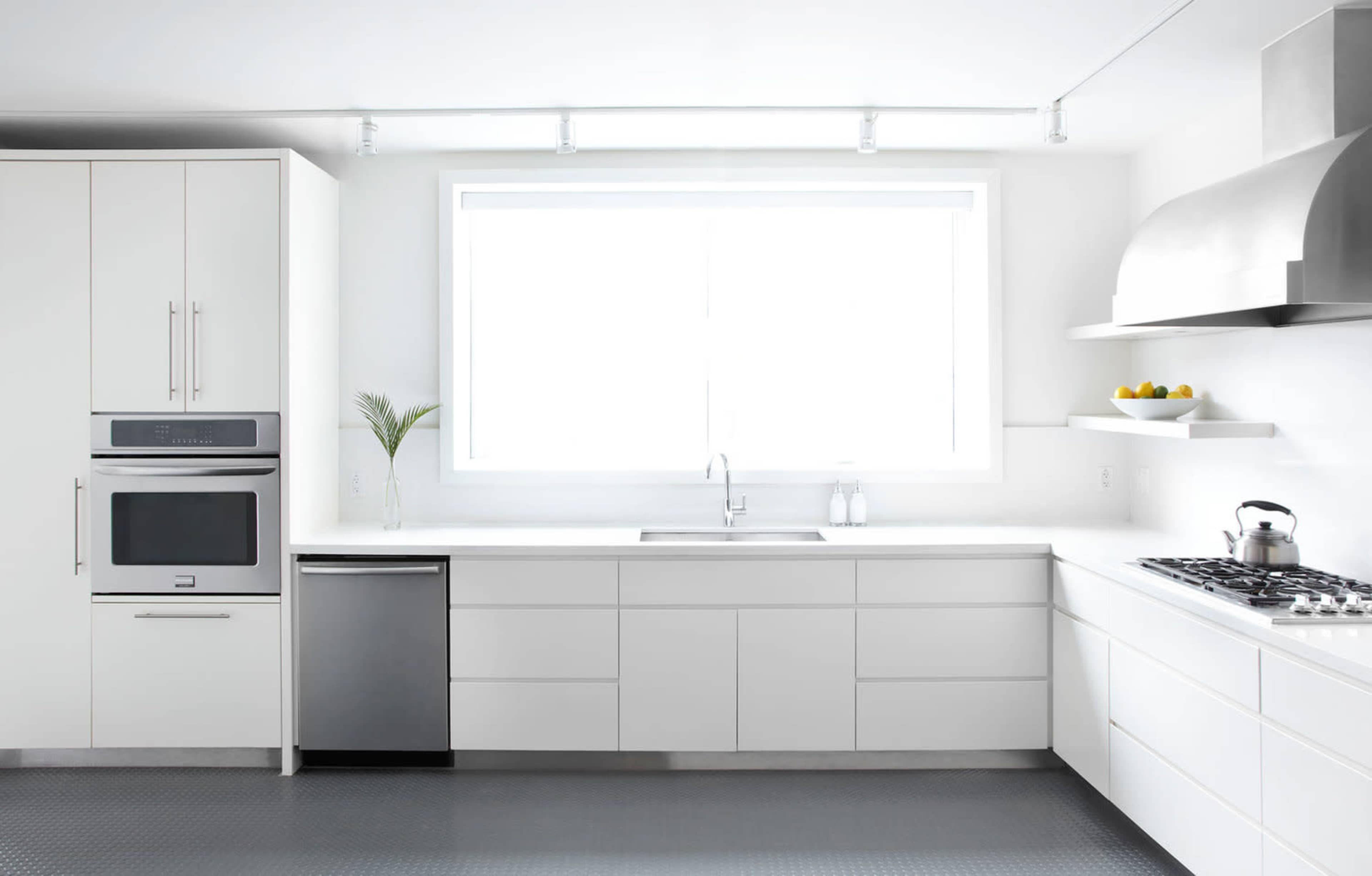 A modern kitchen features white cabinetry, stainless steel appliances, and a large window providing natural light.