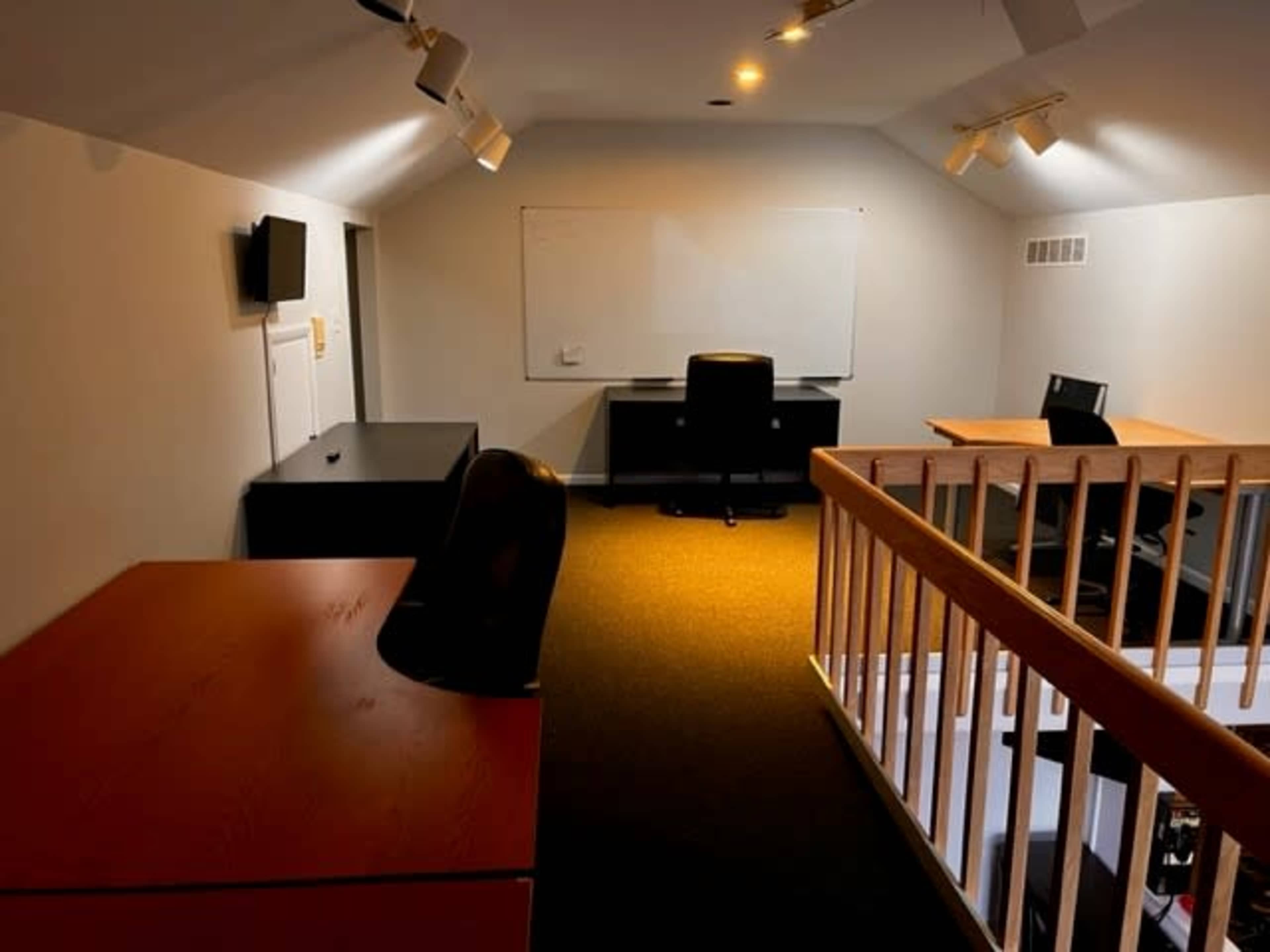 A well-lit office space featuring black and wooden desks, office chairs, and a whiteboard on the wall.