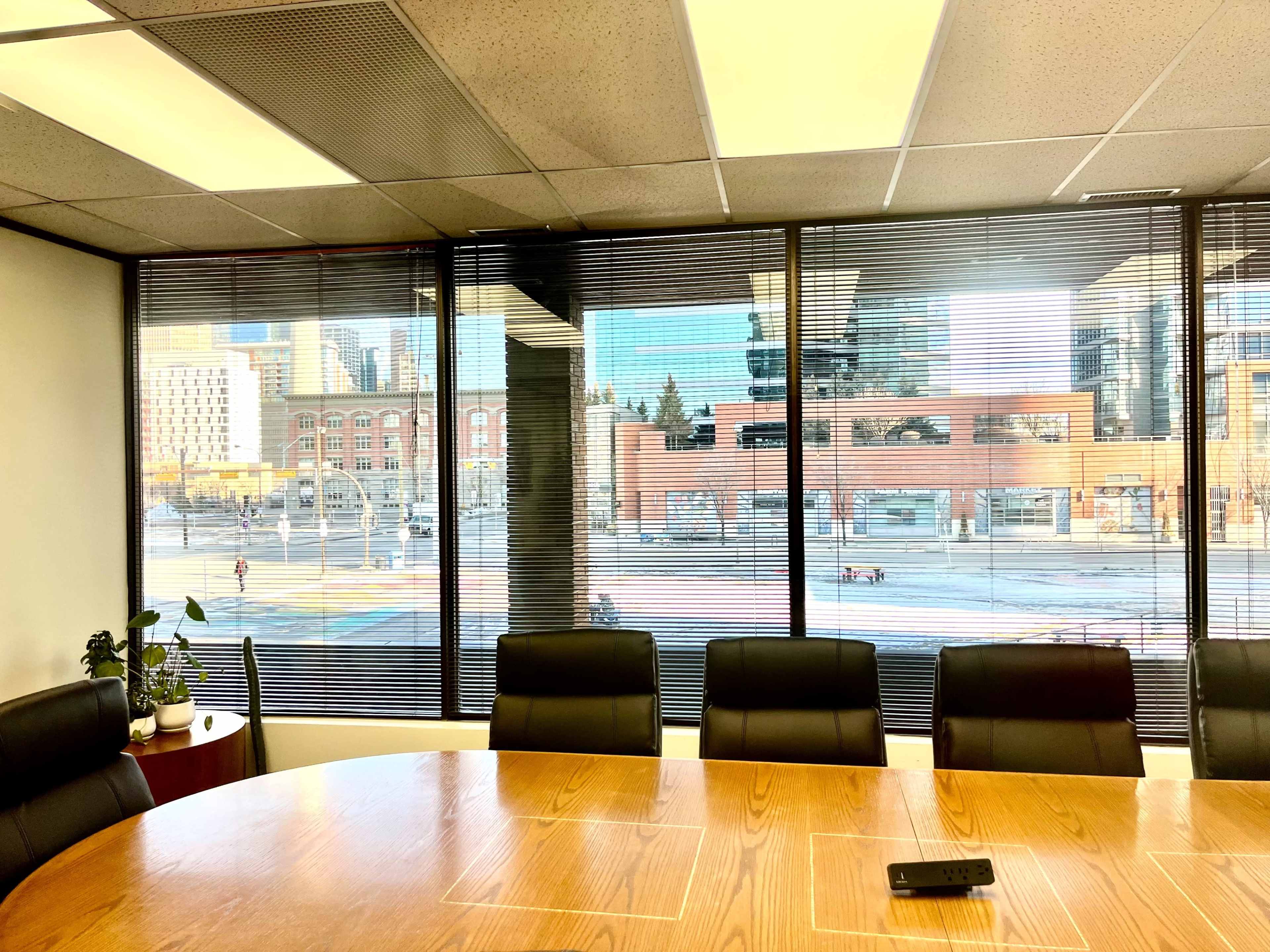A conference room with a wooden table and black chairs features large windows overlooking a cityscape with buildings and a street outside.