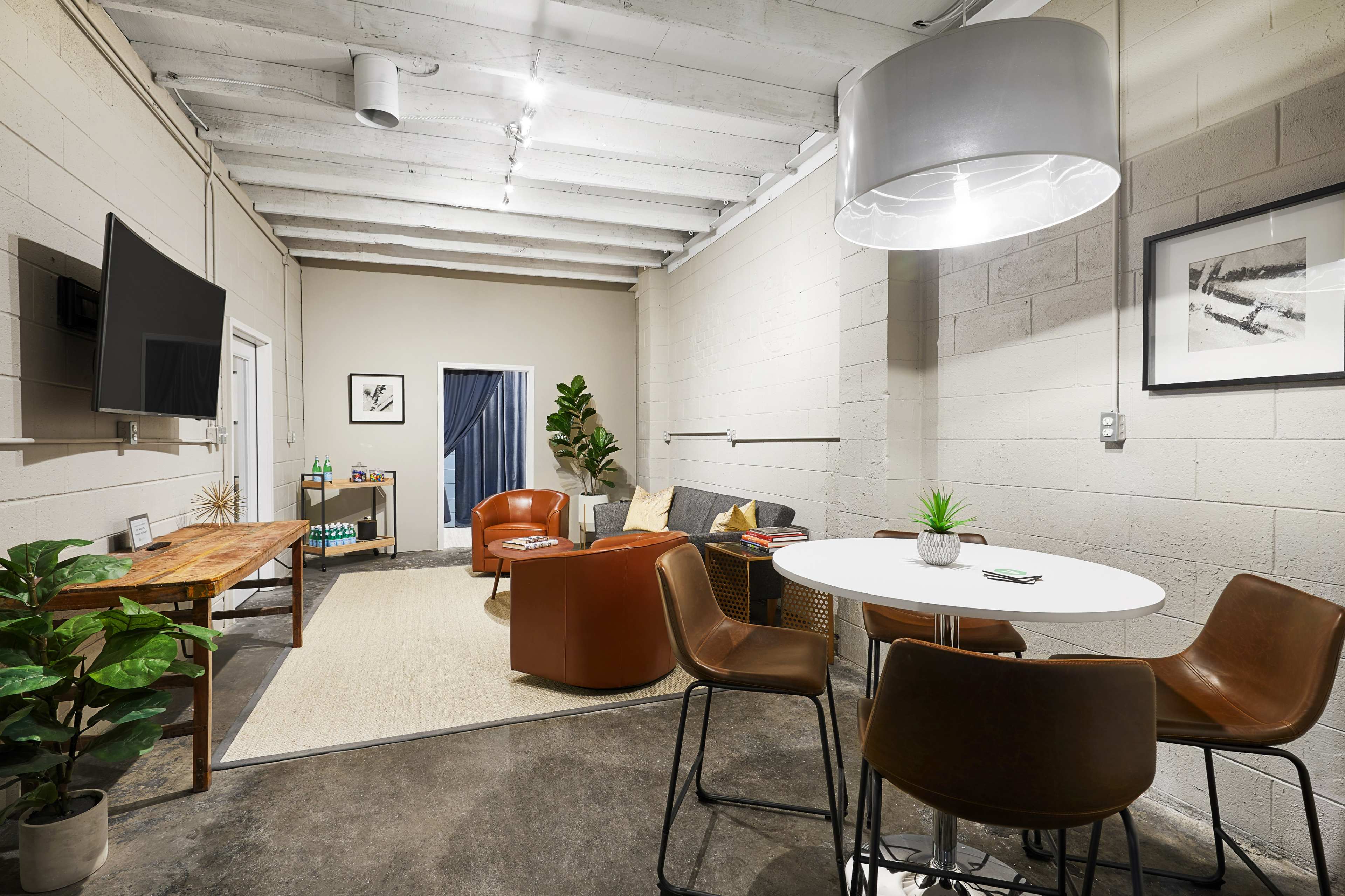 A contemporary office space with a circular table and chairs, a couch, a wooden table, and a large light fixture overhead.