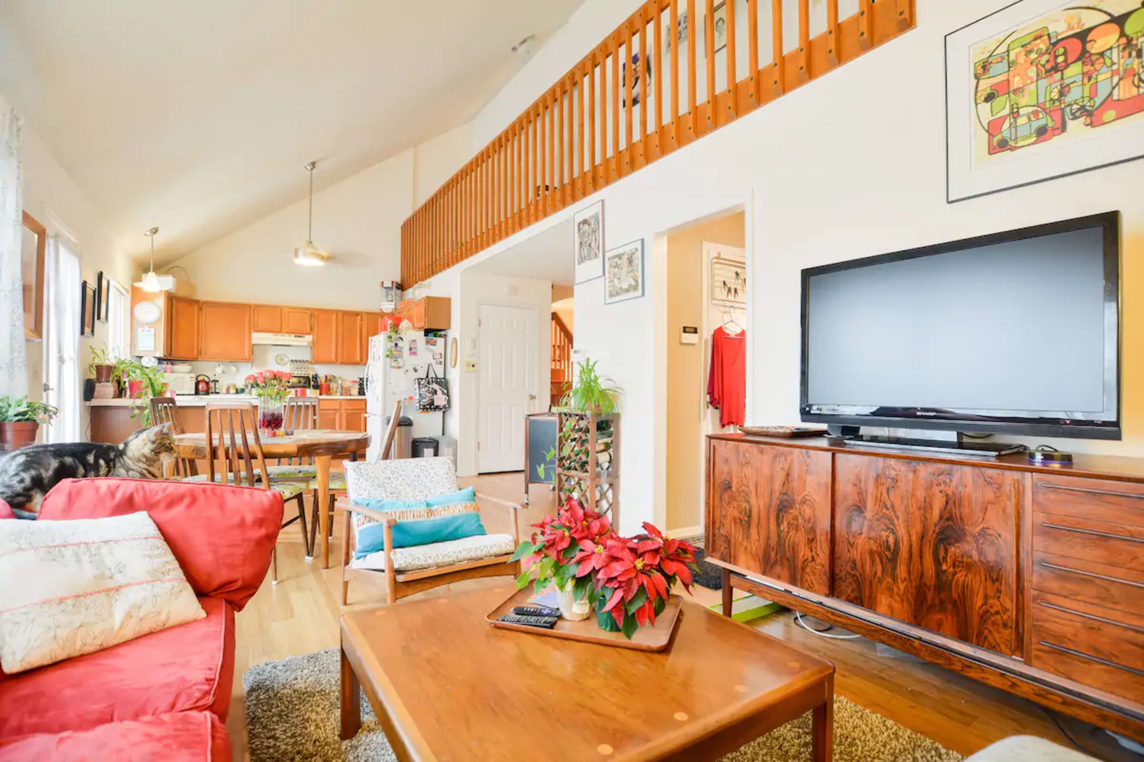 The living area features a red couch and a wooden coffee table, with a TV on a cabinet and a view of an open kitchen in the background.