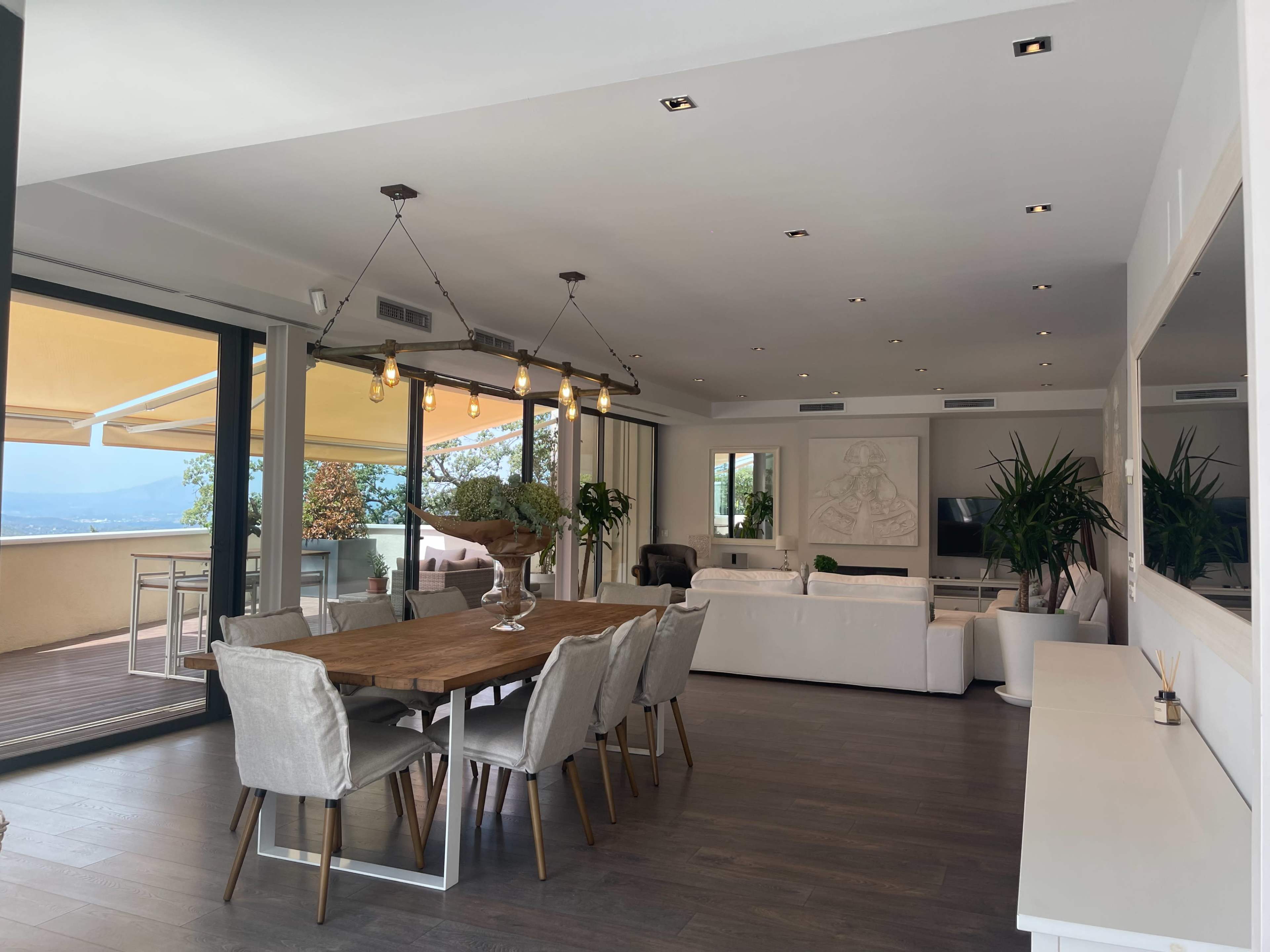A spacious modern living area with a dining table, chairs, and large windows overlooking a scenic view.