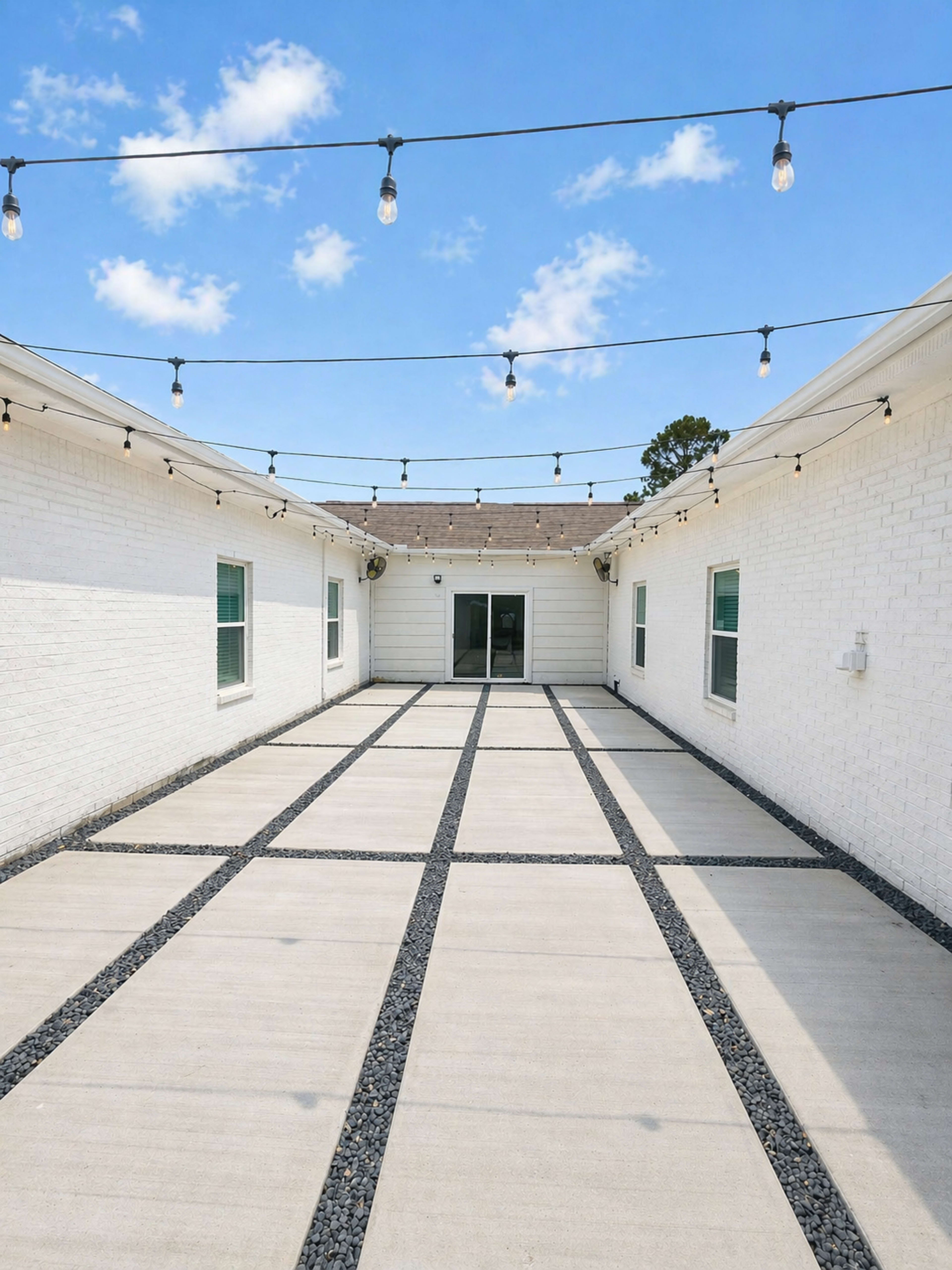 The image shows a wide, paved outdoor area bordered by white walls and illuminated by string lights overhead.