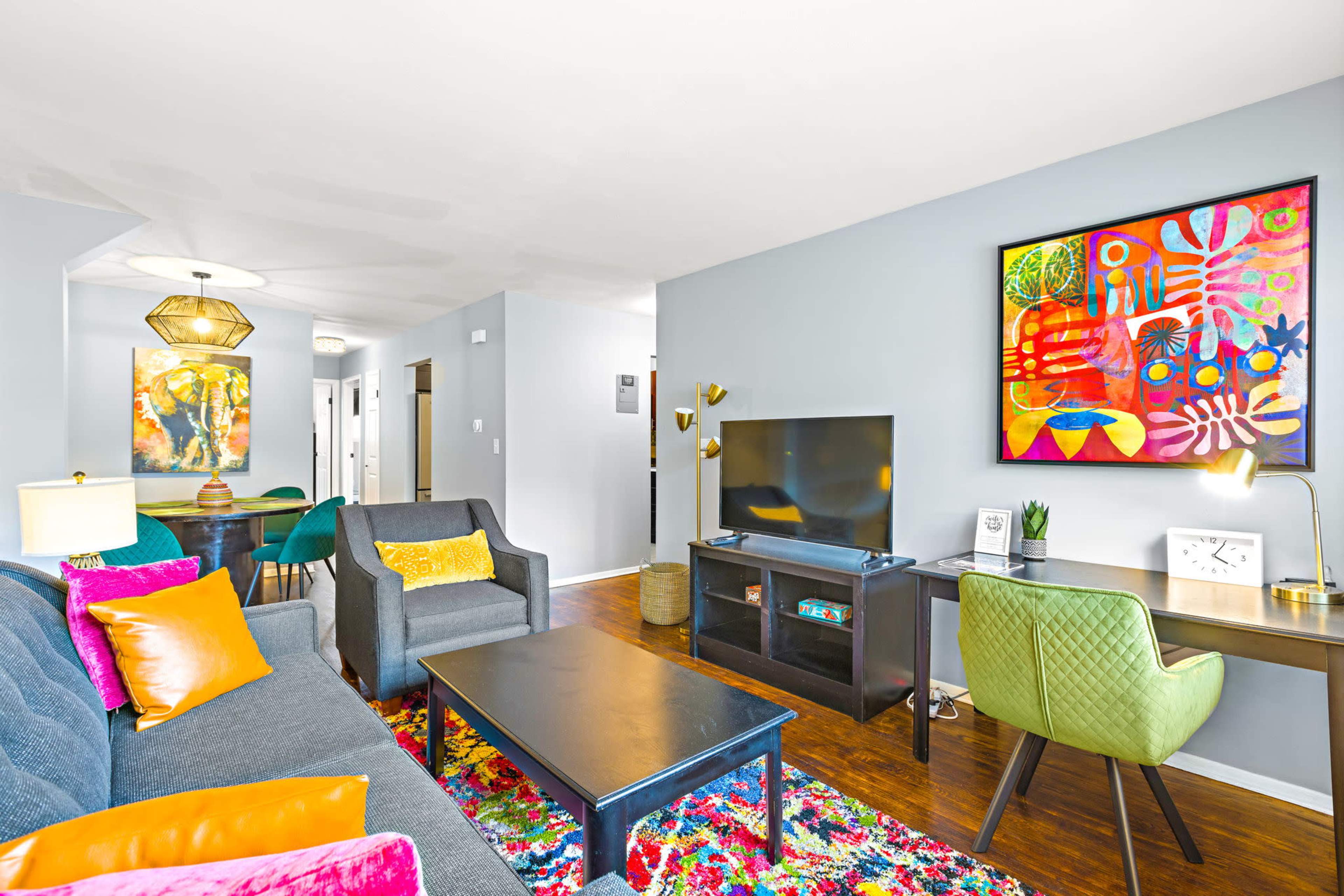 A modern living room with a colorful area rug, a television, a desk, and vibrant artwork on the wall.
