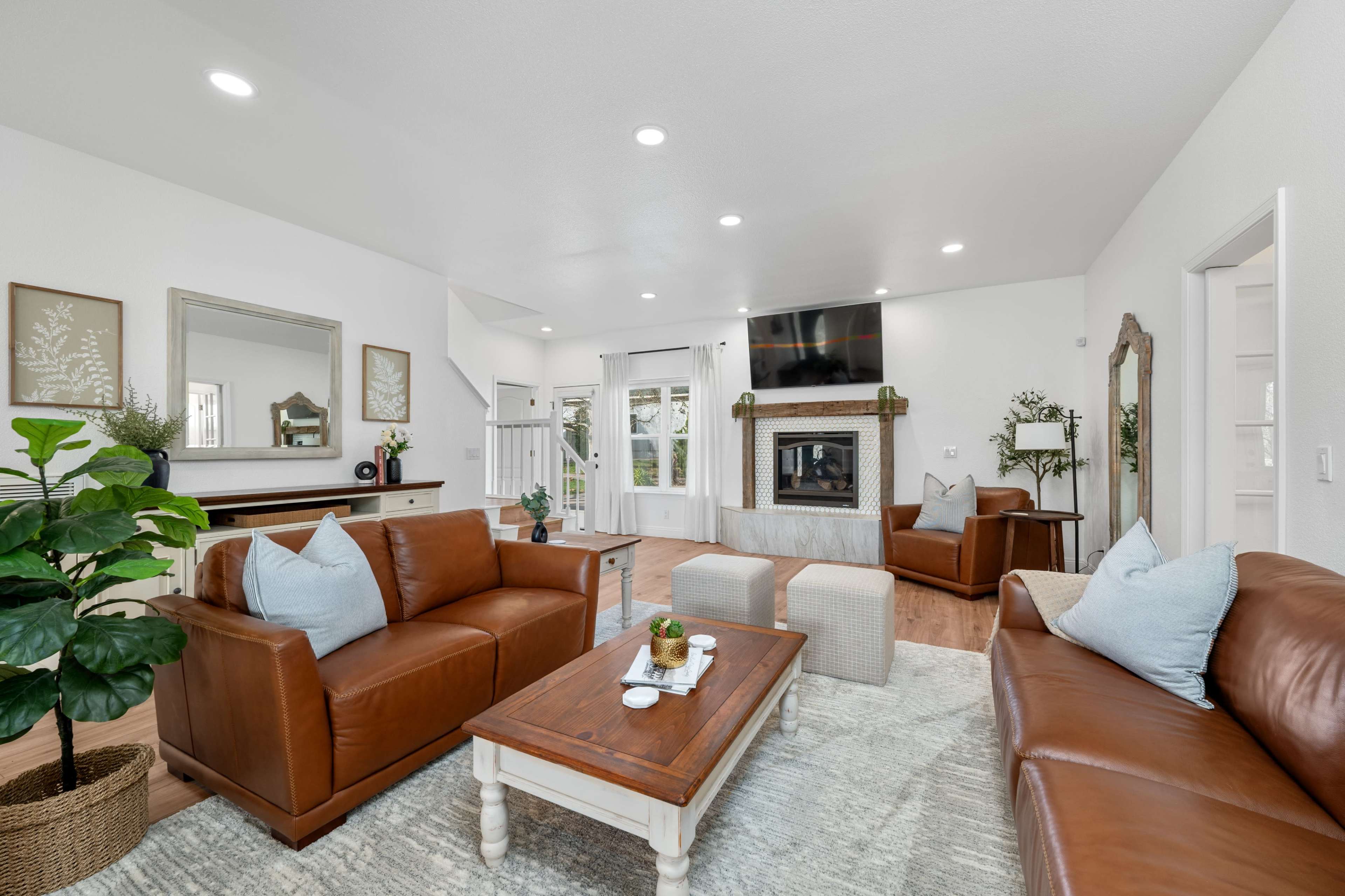 The living room features two leather sofas, a wooden coffee table, and a television mounted above a fireplace, with natural light coming through large windows.