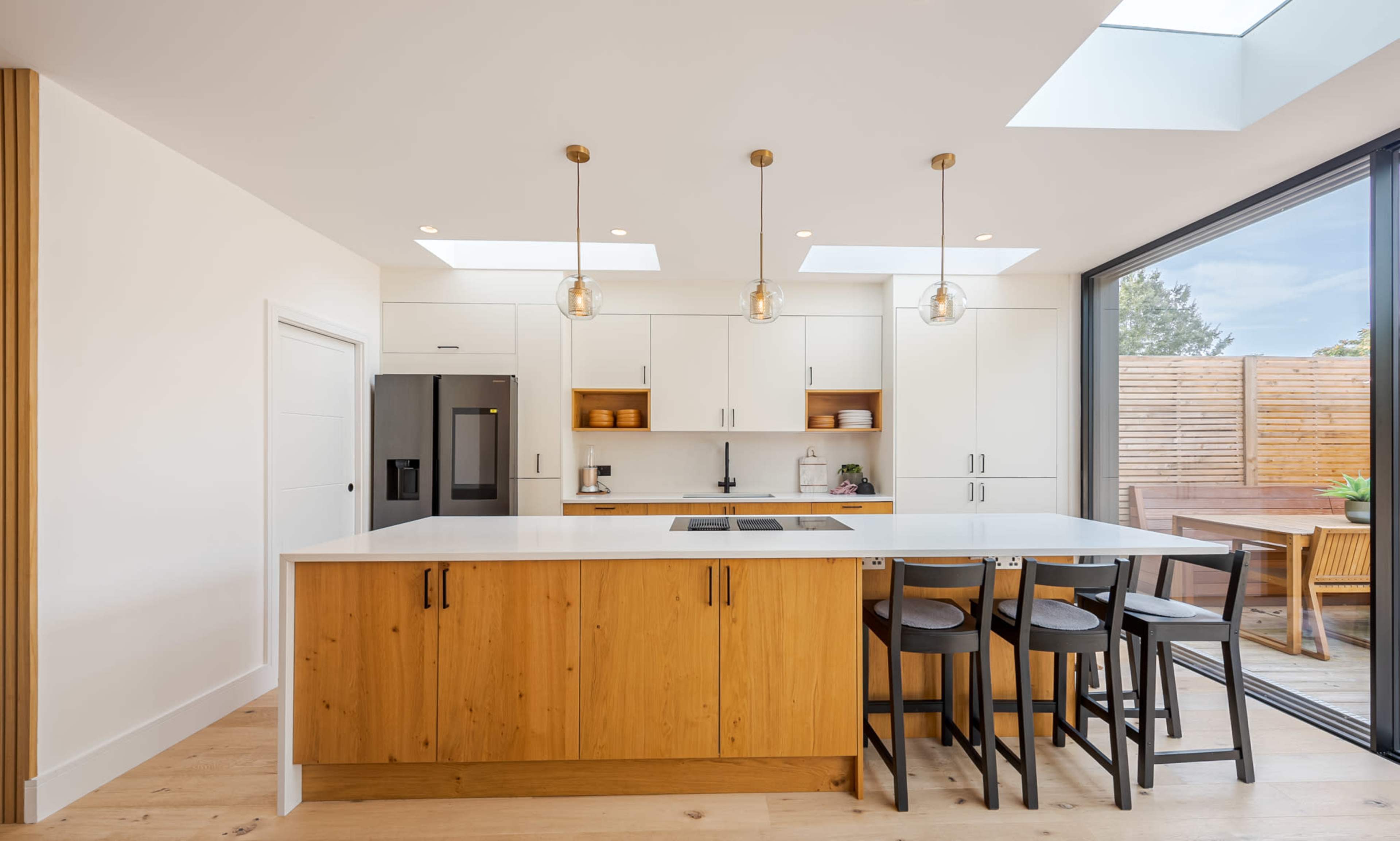 The kitchen features a central island with wooden cabinetry, overhead pendant lights, and large windows that provide natural light.