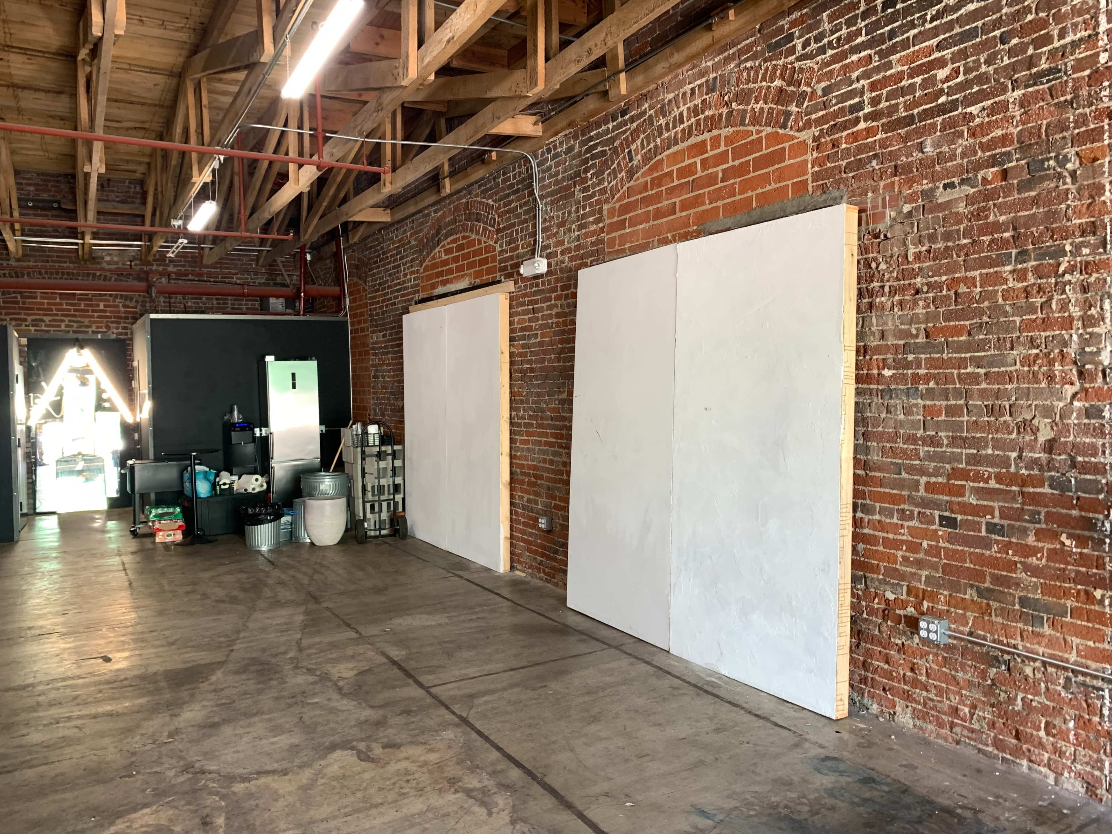 The image shows an industrial space with exposed brick walls, two blank white panels, and various items stored along the side.