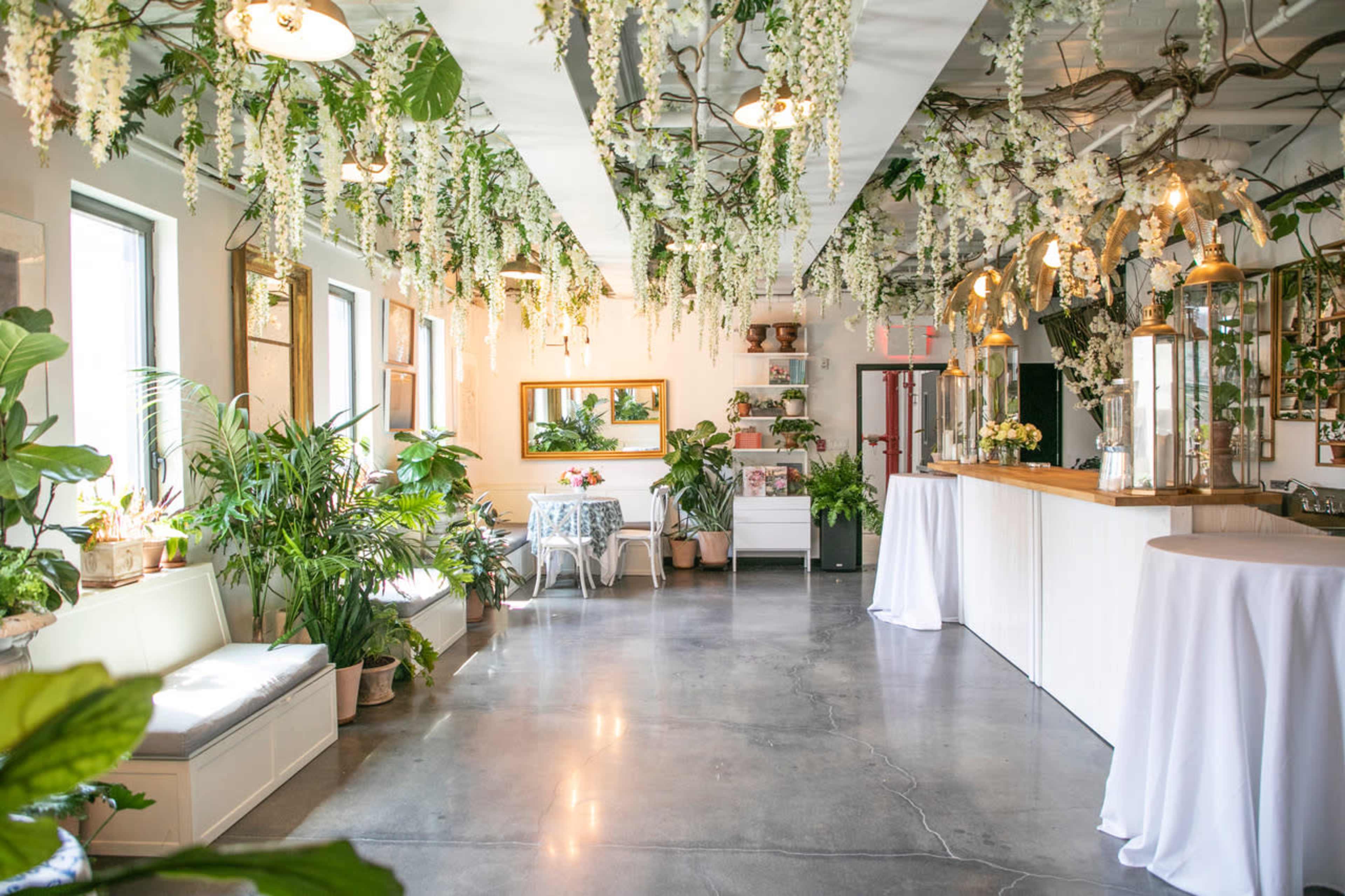 A bright indoor space adorned with hanging flowers and greenery, featuring seating areas and a wooden counter.