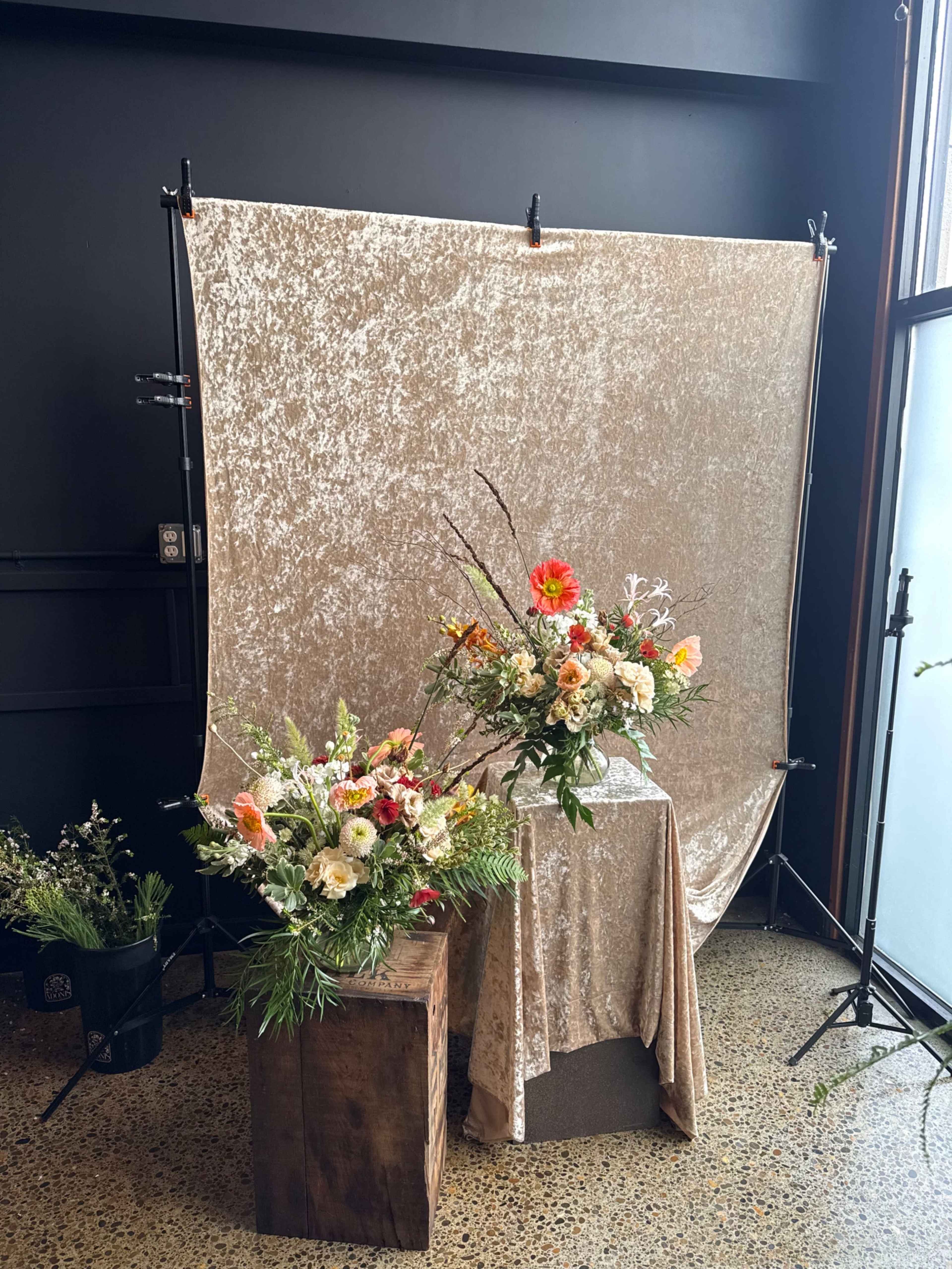 The image features a floral arrangement displayed in front of a textured, golden backdrop, with a small table draped in a matching fabric.