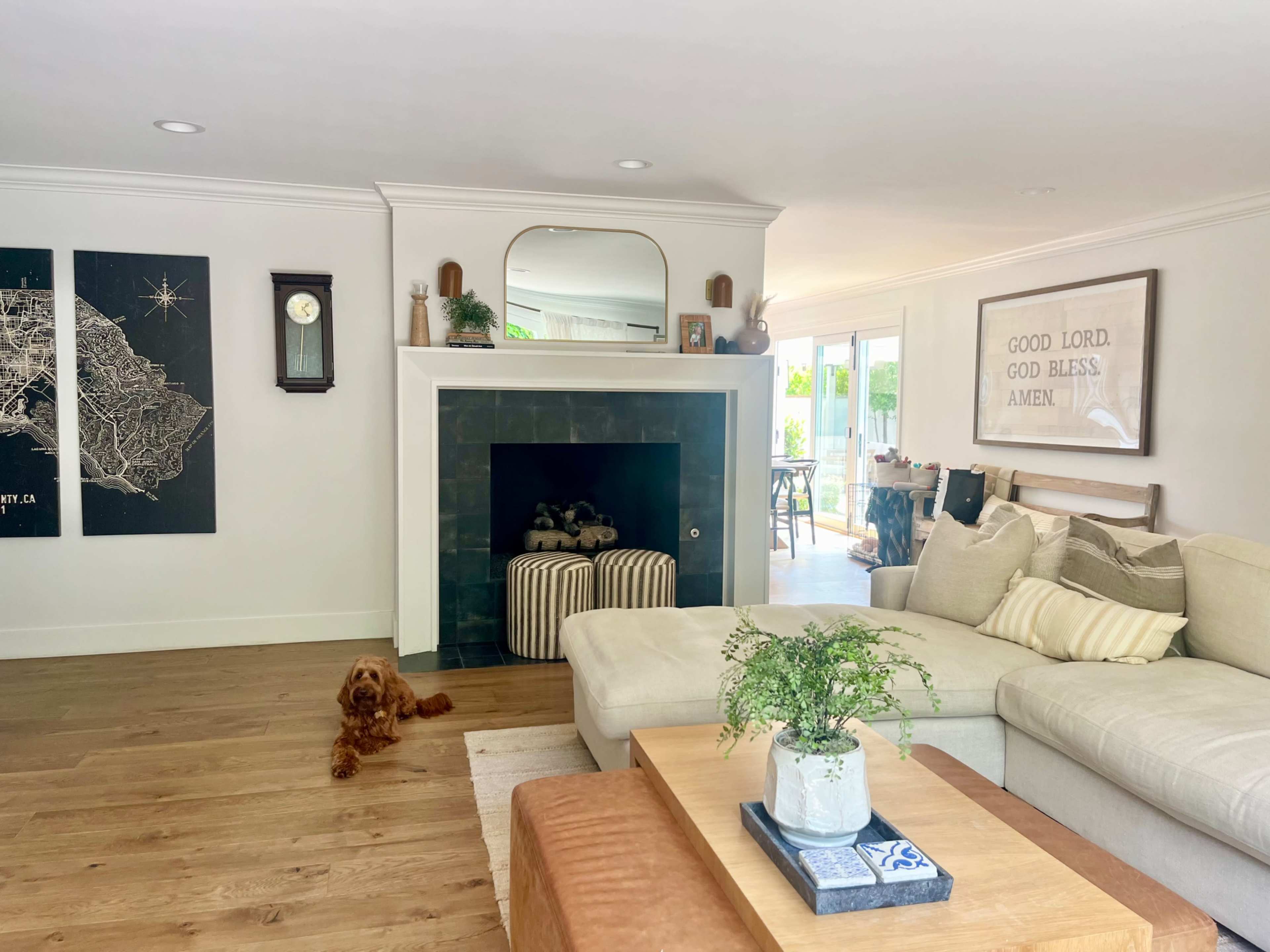 A cozy living room features a sectional sofa, a wooden coffee table, and a fireplace, with a clock on the wall and a dog resting on the floor.