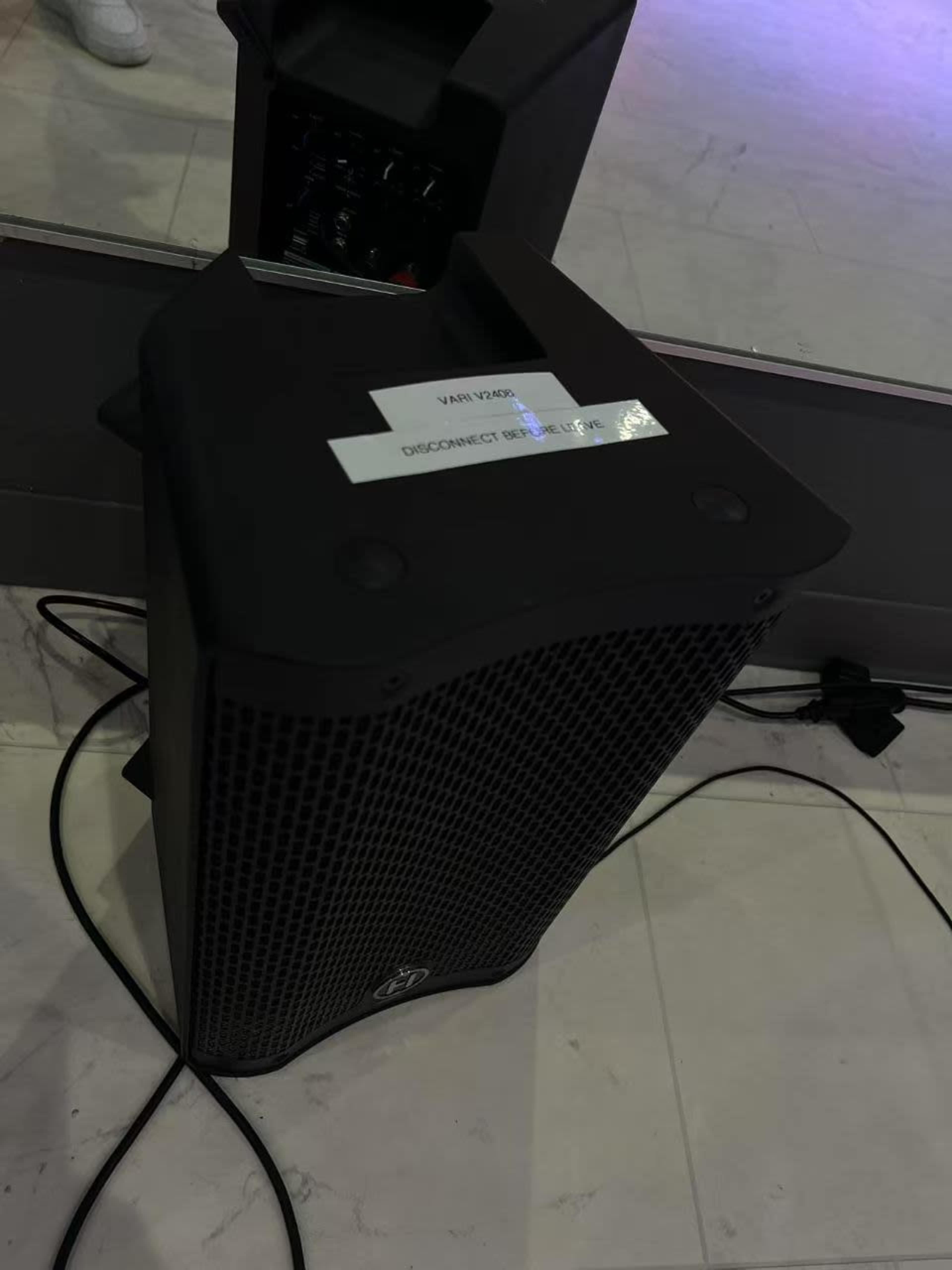 A black speaker is positioned on the floor near a wall with visible cables surrounding it.