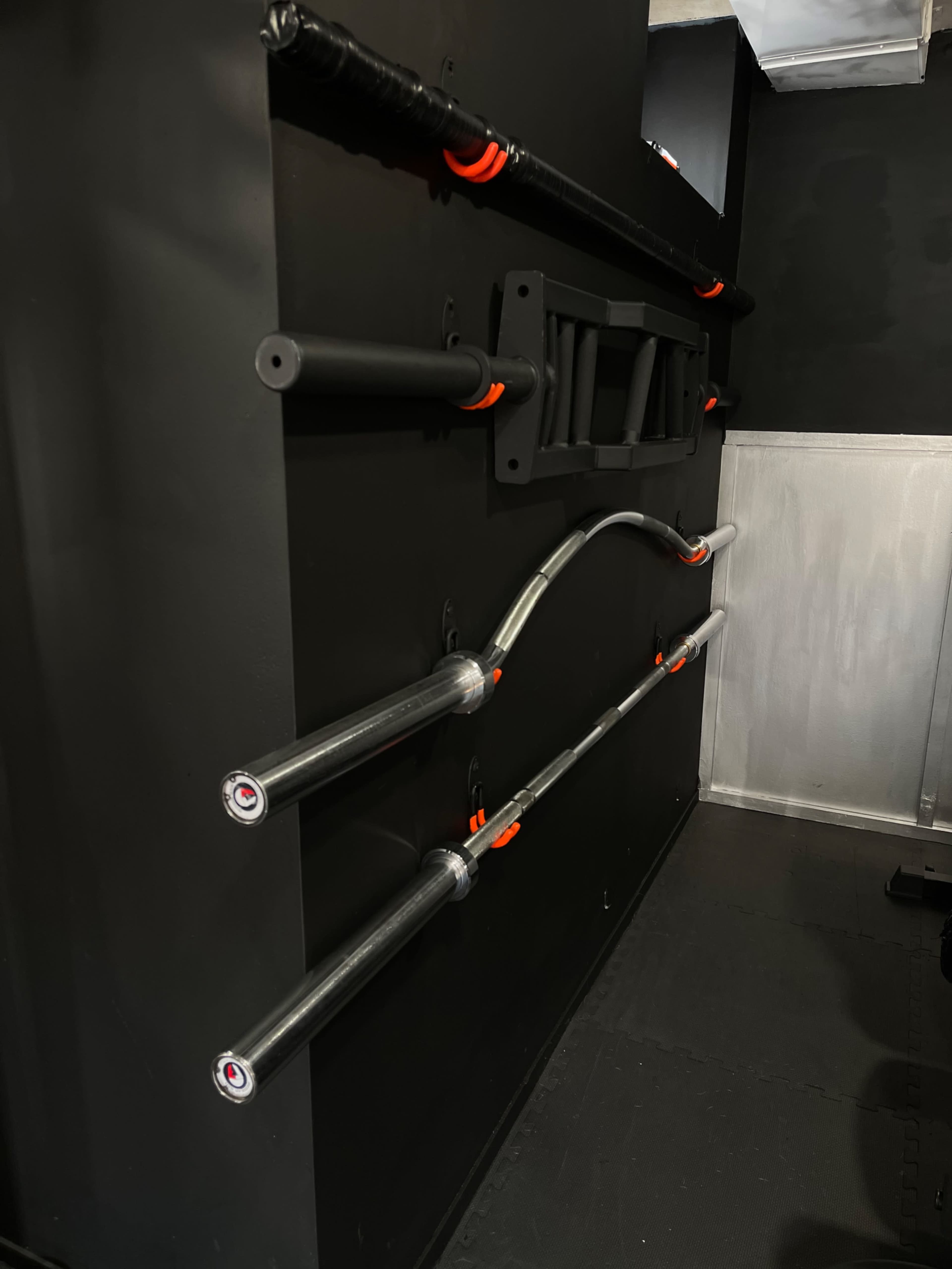 A black wall with a set of metal bars and attachments for exercise equipment.