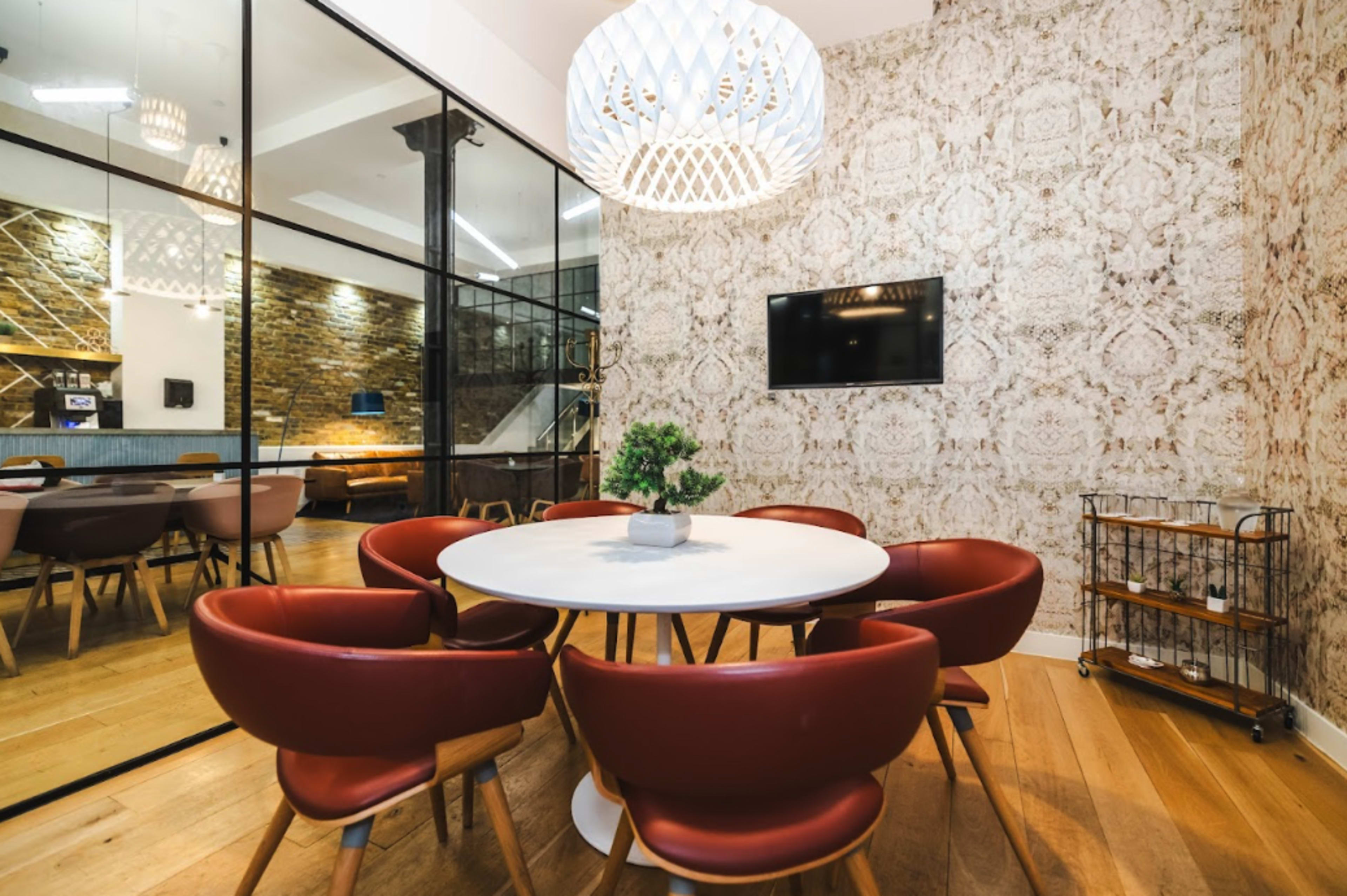 A modern meeting room features a round table surrounded by leather chairs, with a decorative wall and a pendant light above.