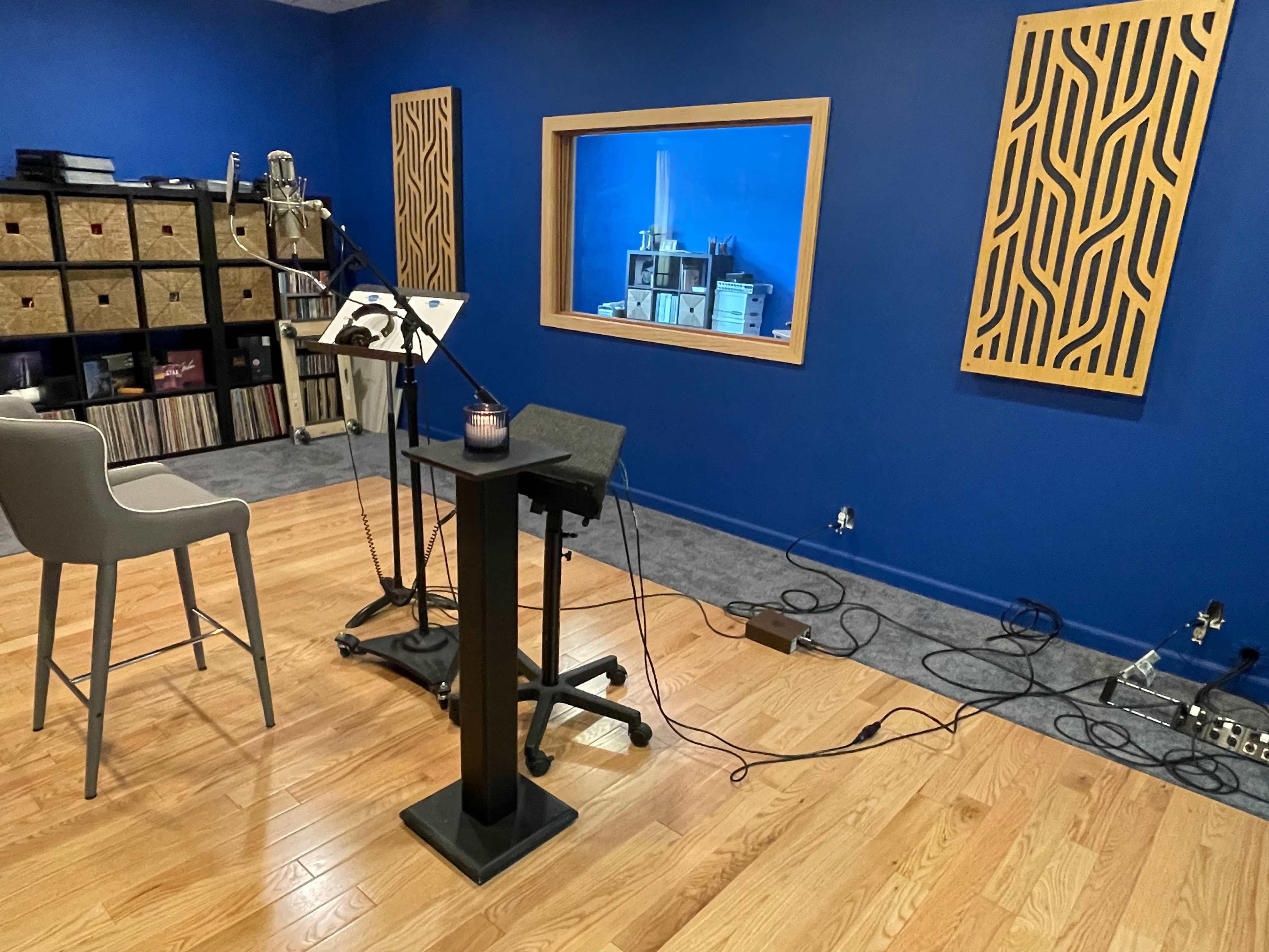 A recording studio with a microphone setup, a chair, and sound-absorbing panels on blue walls.