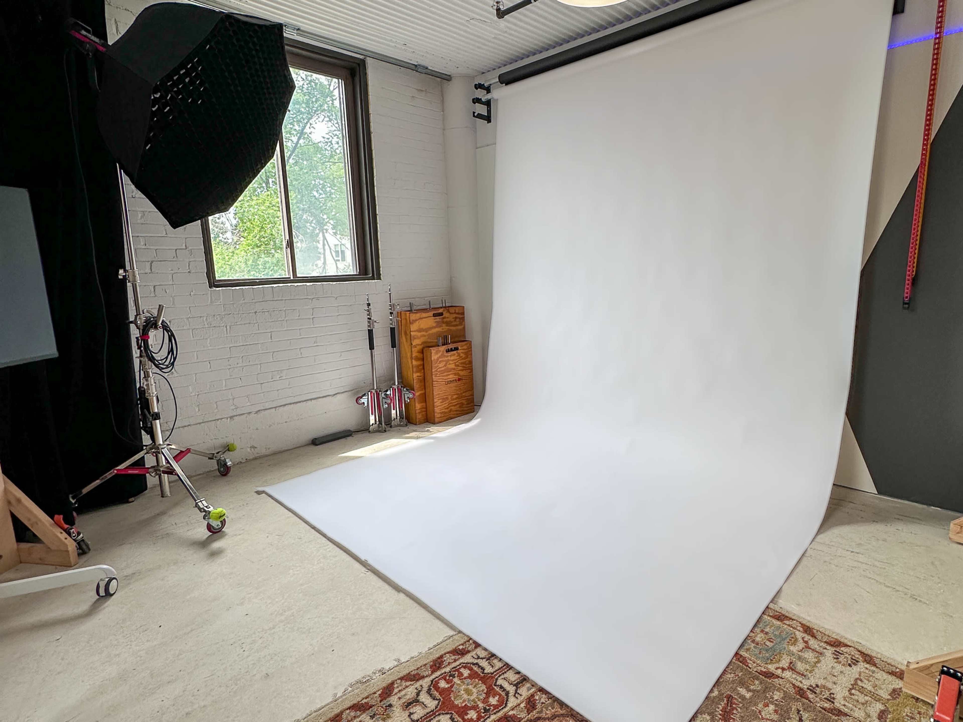 A photography studio with a large white backdrop, a softbox light, and various studio equipment arranged nearby.