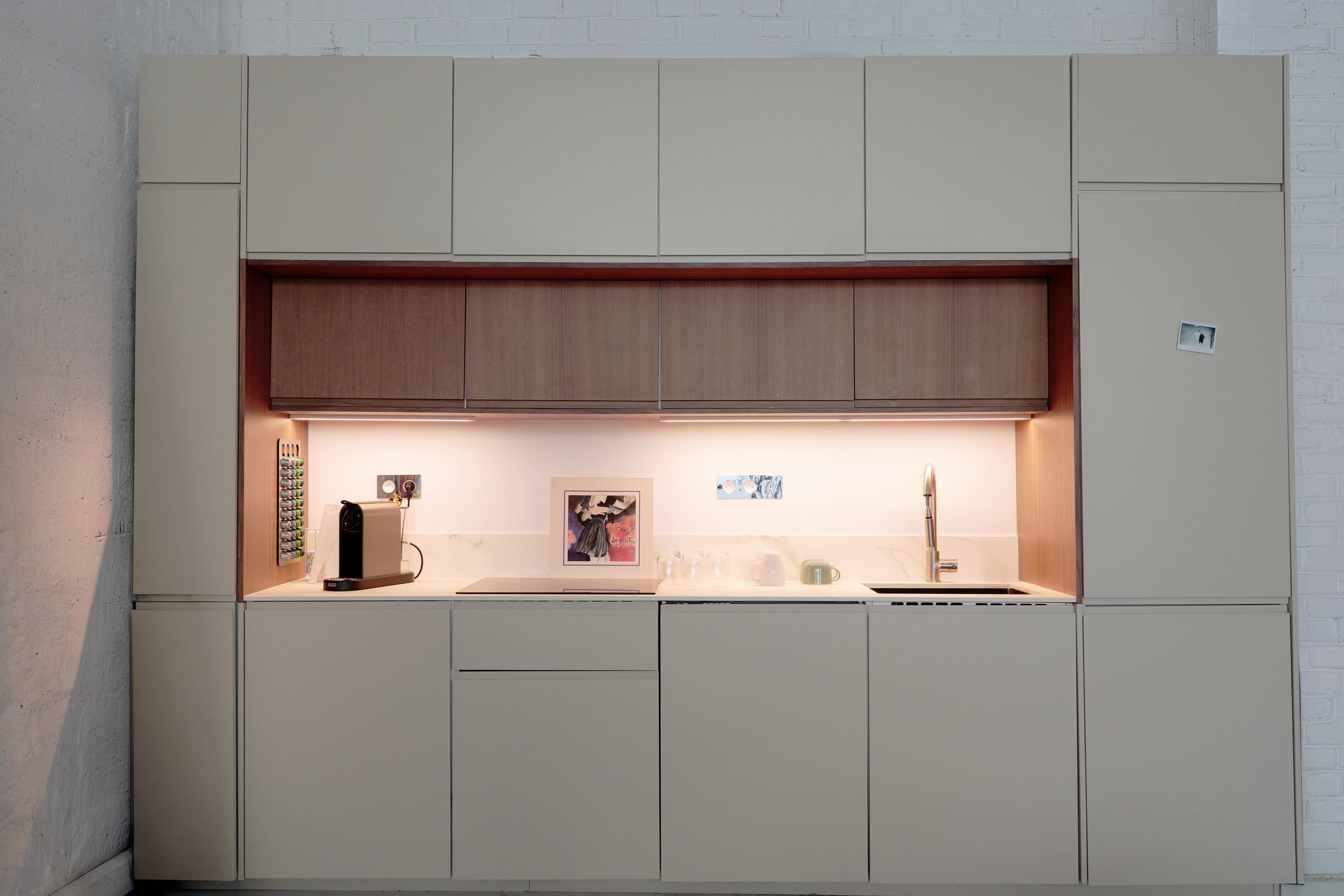 The image shows a modern kitchen with beige cabinets, a wooden countertop, and integrated appliances, featuring a sink and a framed picture on the counter.