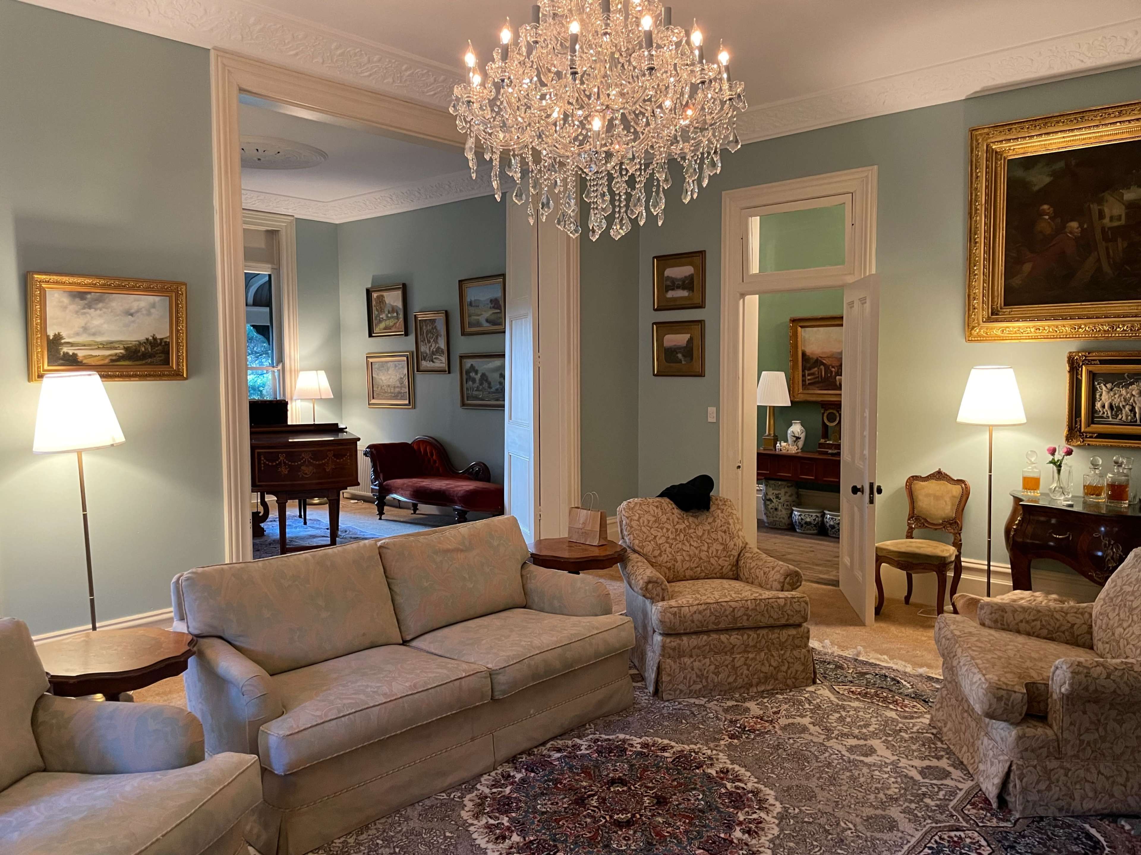 A tastefully furnished living room with a chandelier, several light fixtures, and paintings on the walls, featuring a plush rug in the center.