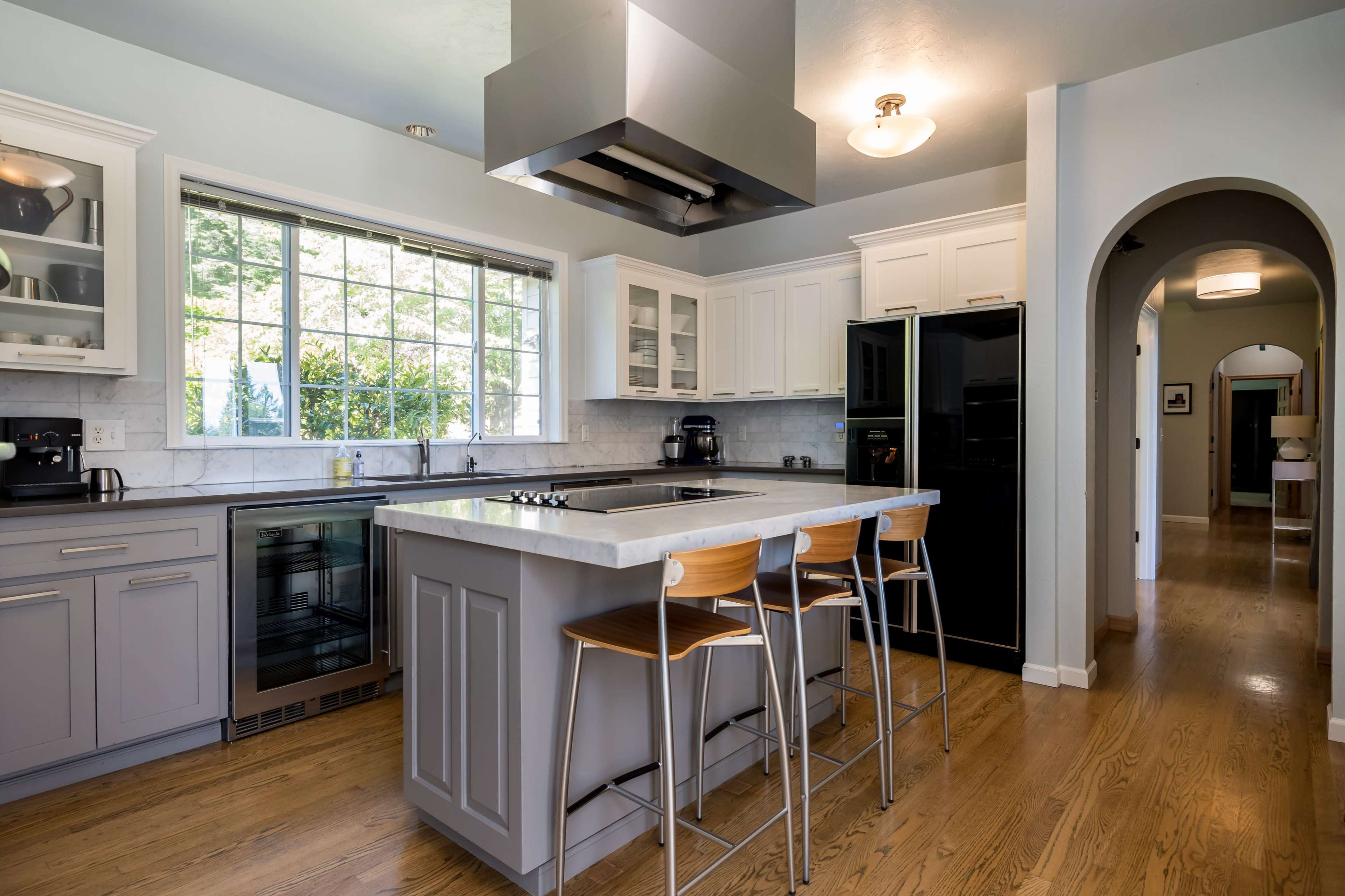 A modern kitchen features a central island with seating, stainless steel appliances, and large windows allowing natural light to enter.