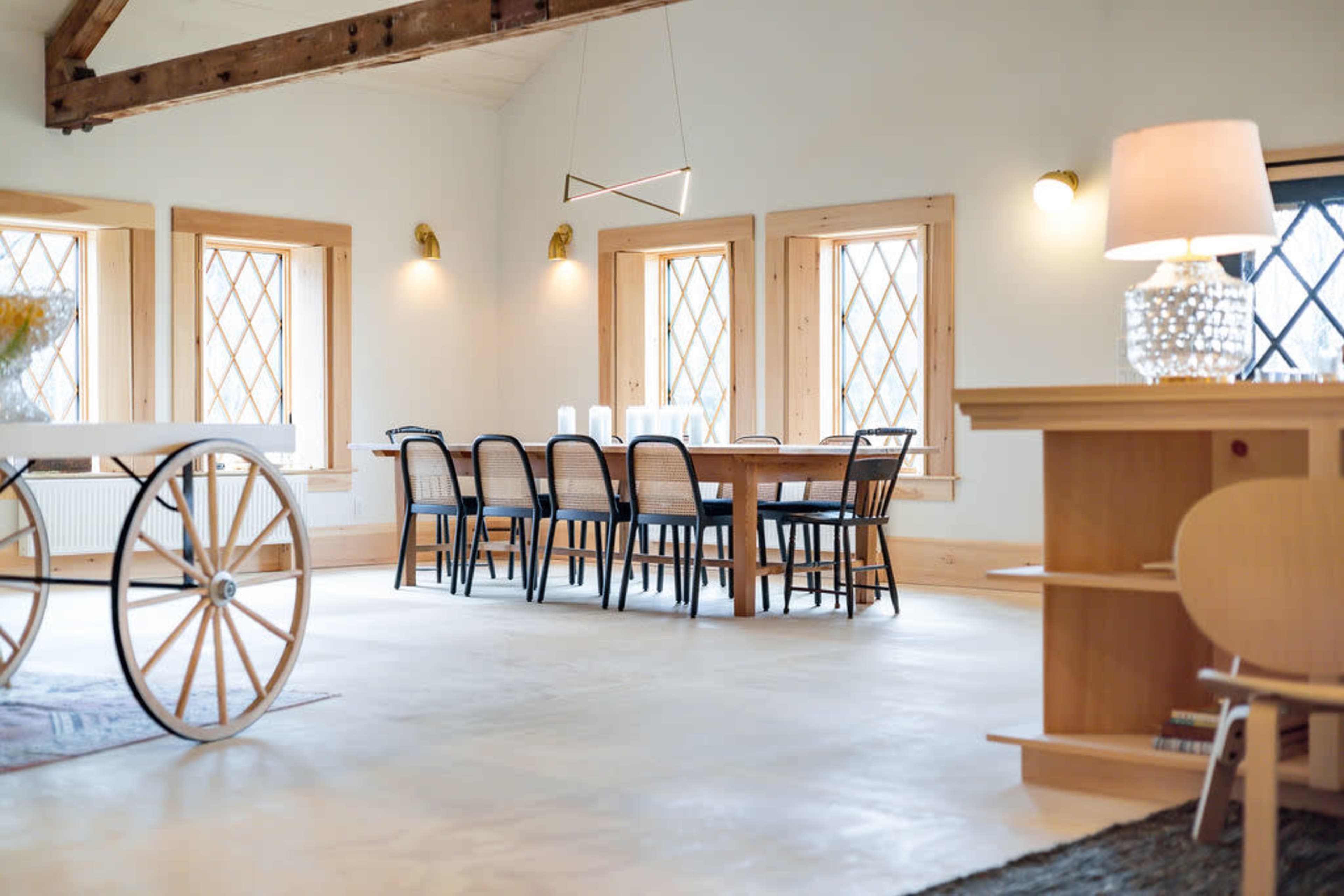 A spacious dining area featuring a long wooden table surrounded by black chairs, with large windows and wooden accents throughout.