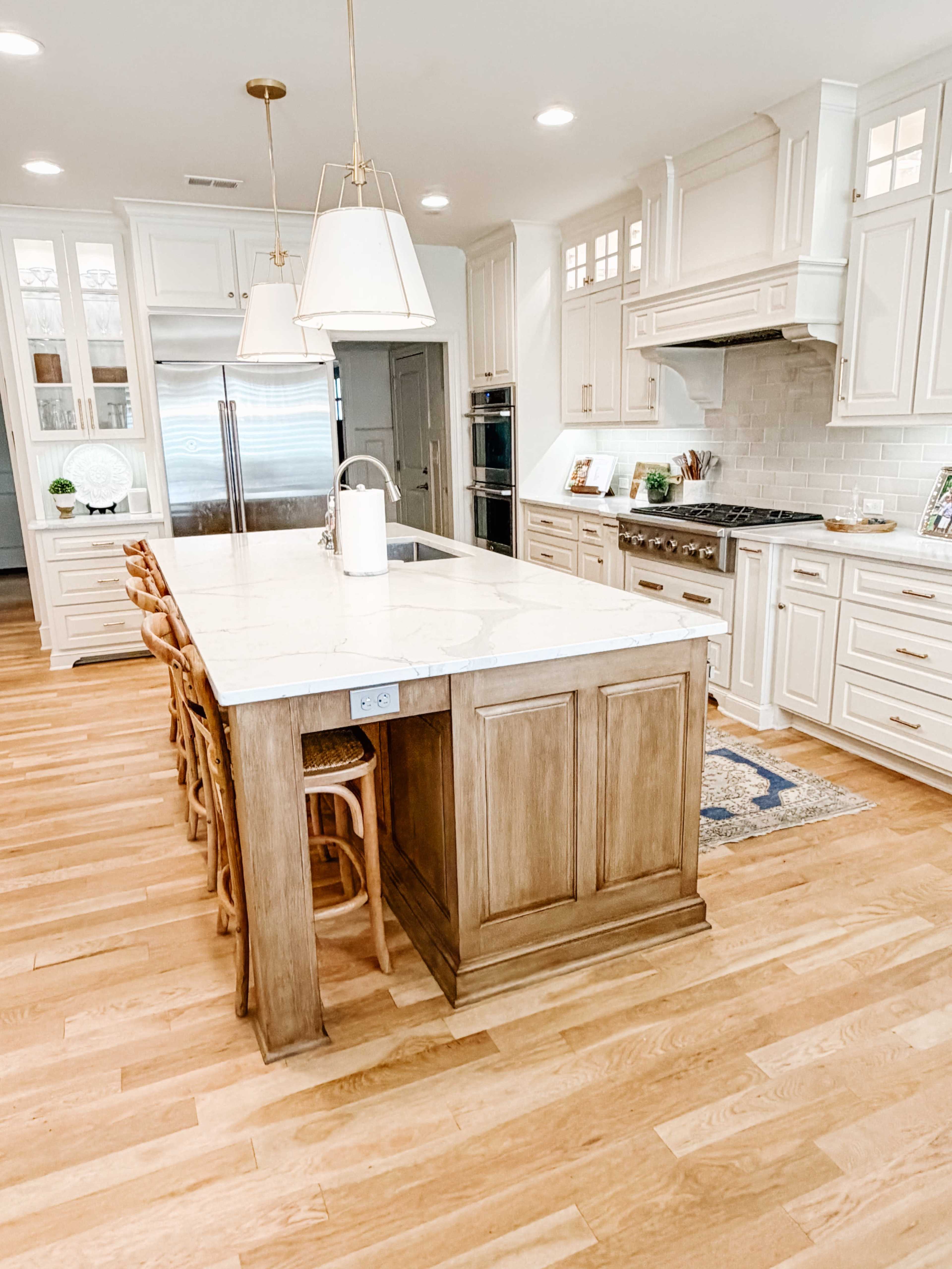 The kitchen features a large central island with wood accents, surrounded by stools, with white cabinetry and marble countertops.