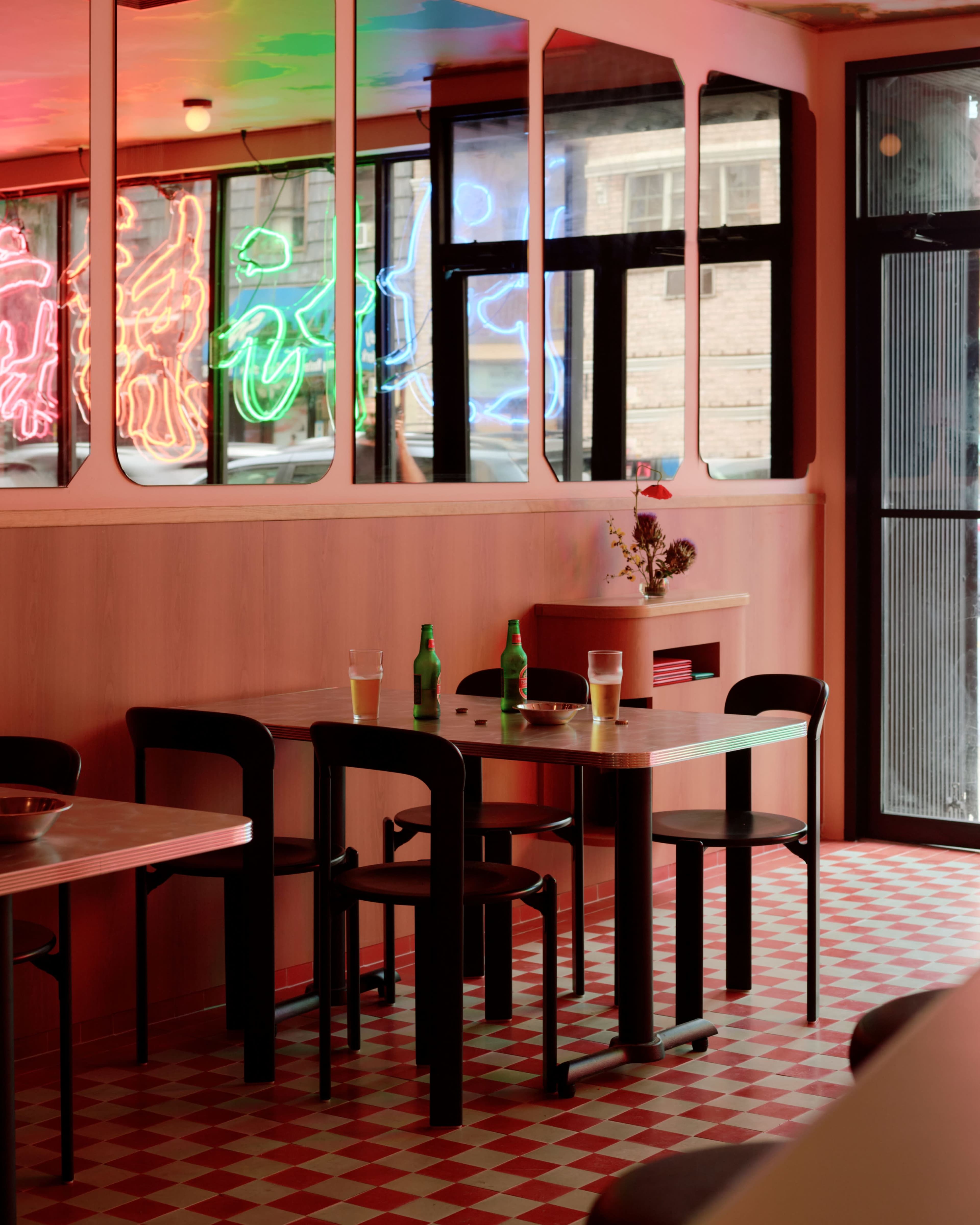 A bright restaurant interior features tables with drinks and colorful neon signs visible through the windows.