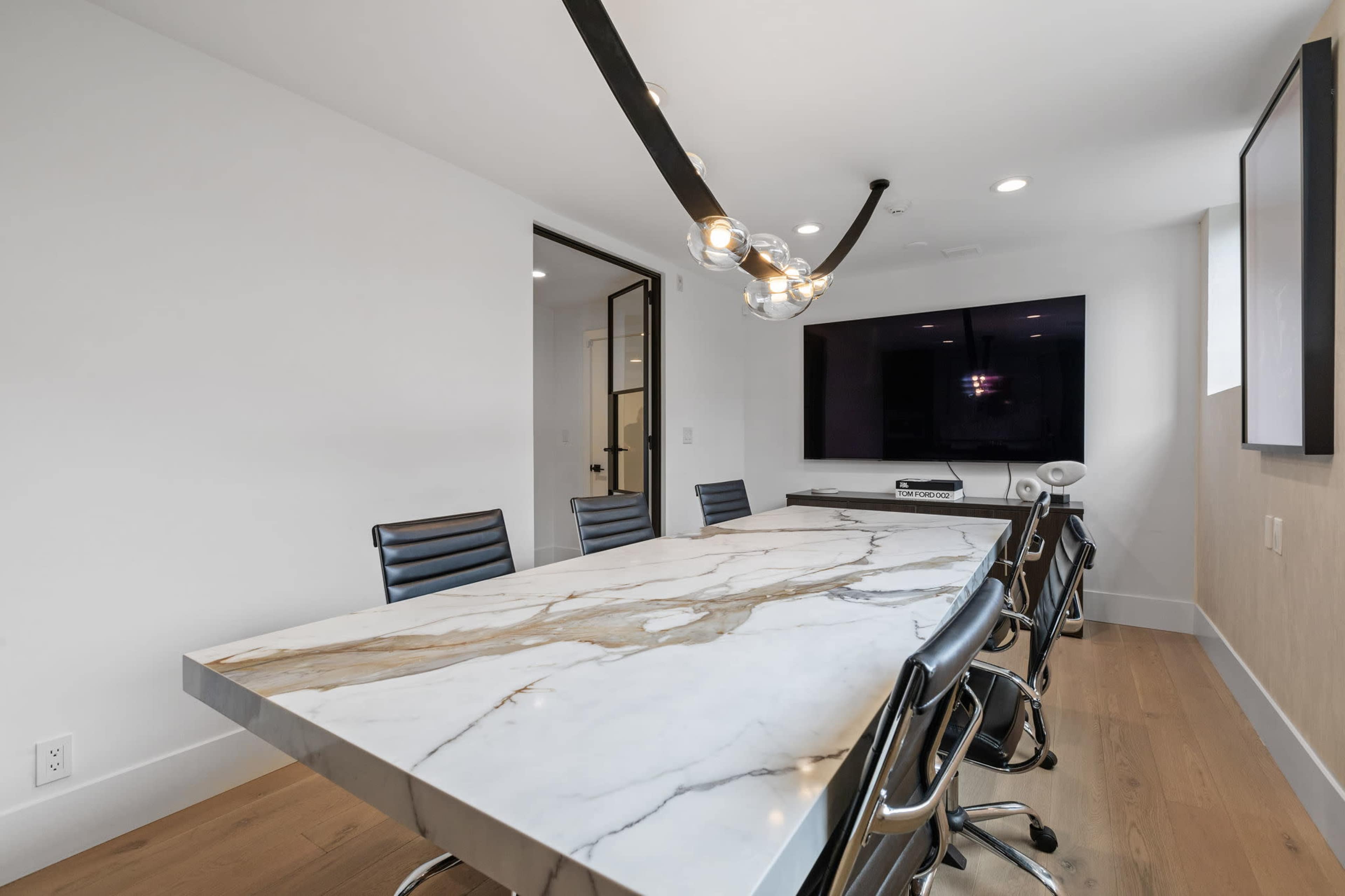 A modern conference room features a long marble table, black chairs, and a wall-mounted television.