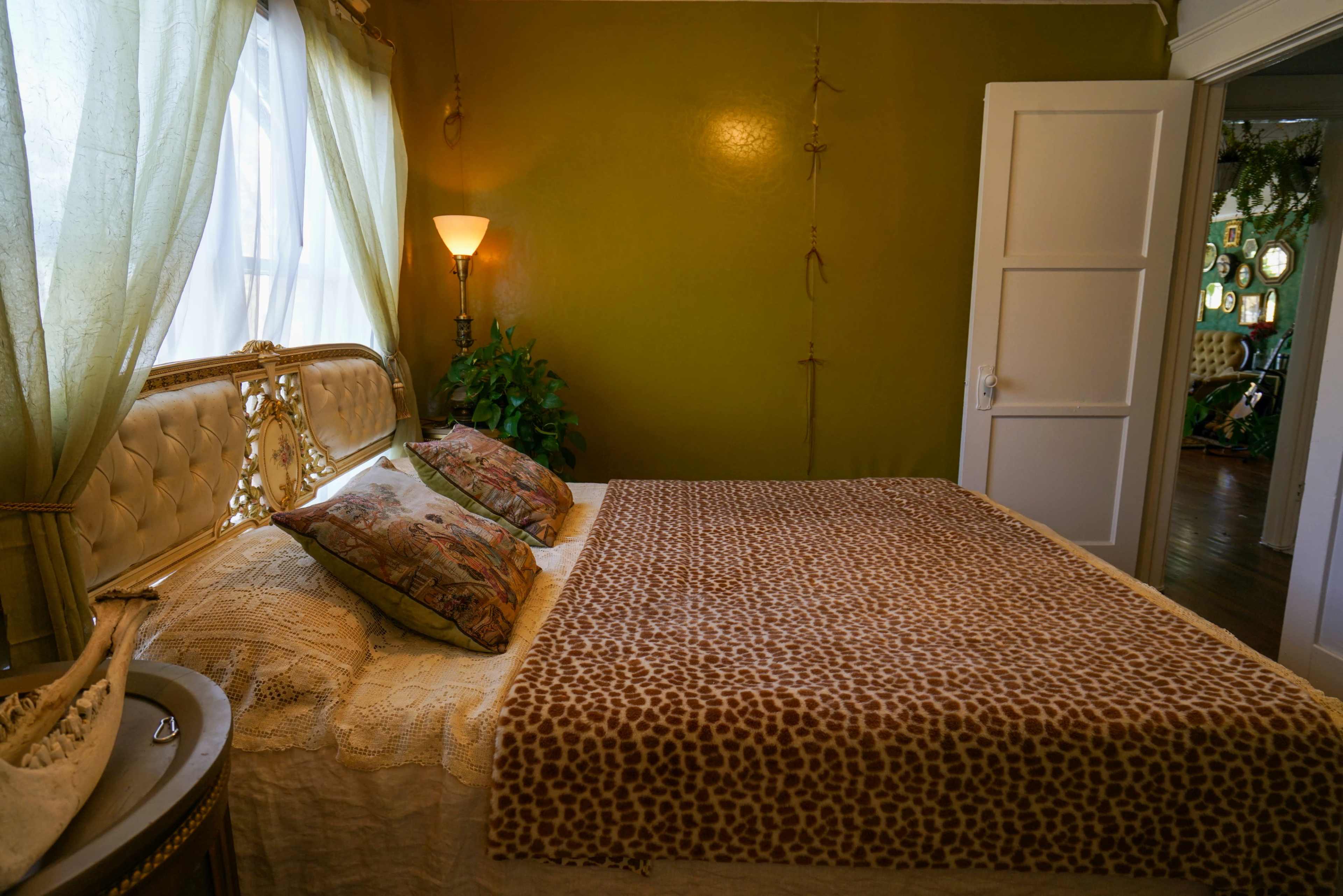 A cozy bedroom with a large bed covered in a leopard-print blanket, flanked by green curtains and a floor lamp.