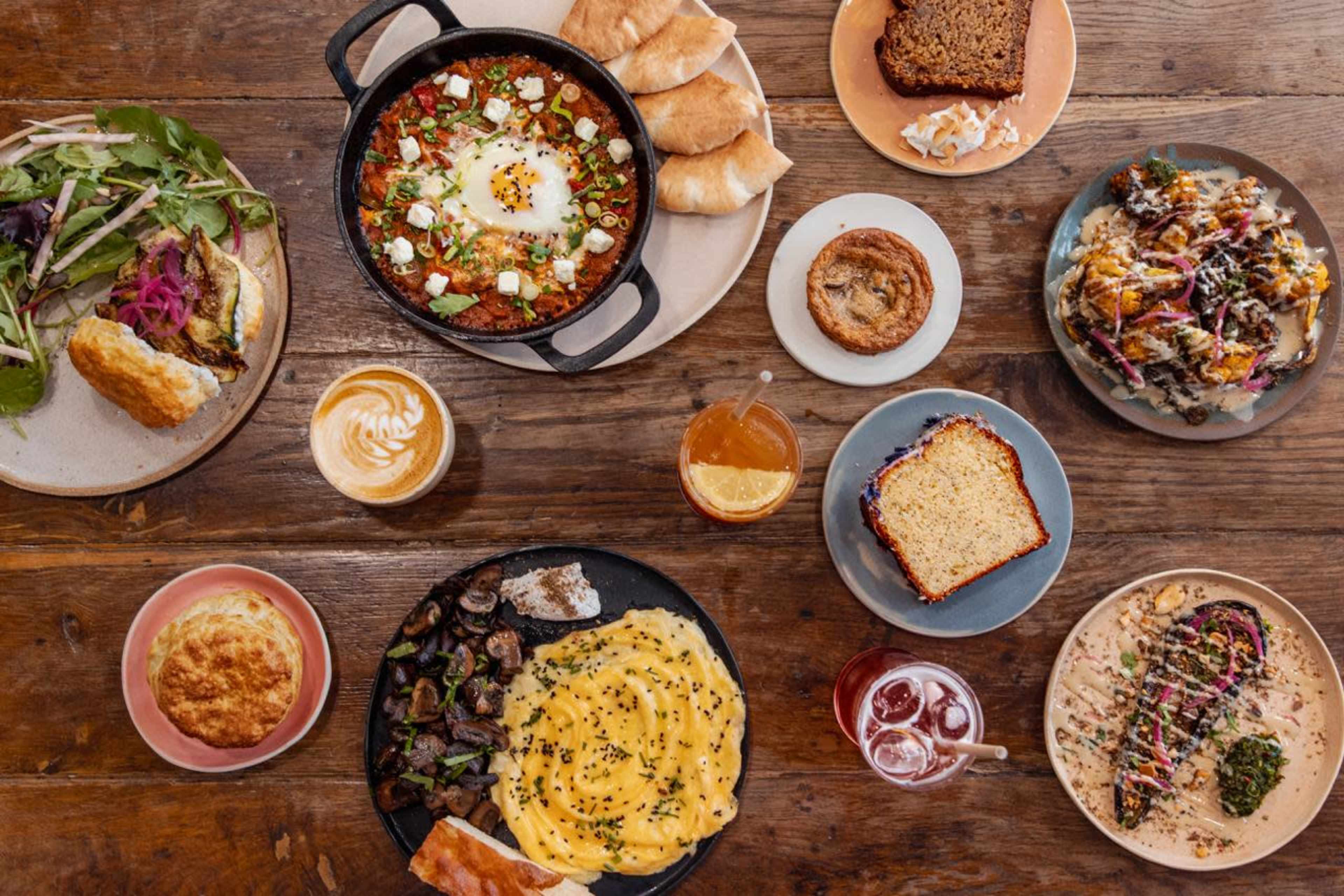 The image showcases a variety of dishes on a wooden table, including a cast-iron skillet with eggs, baked goods, and colorful salads.