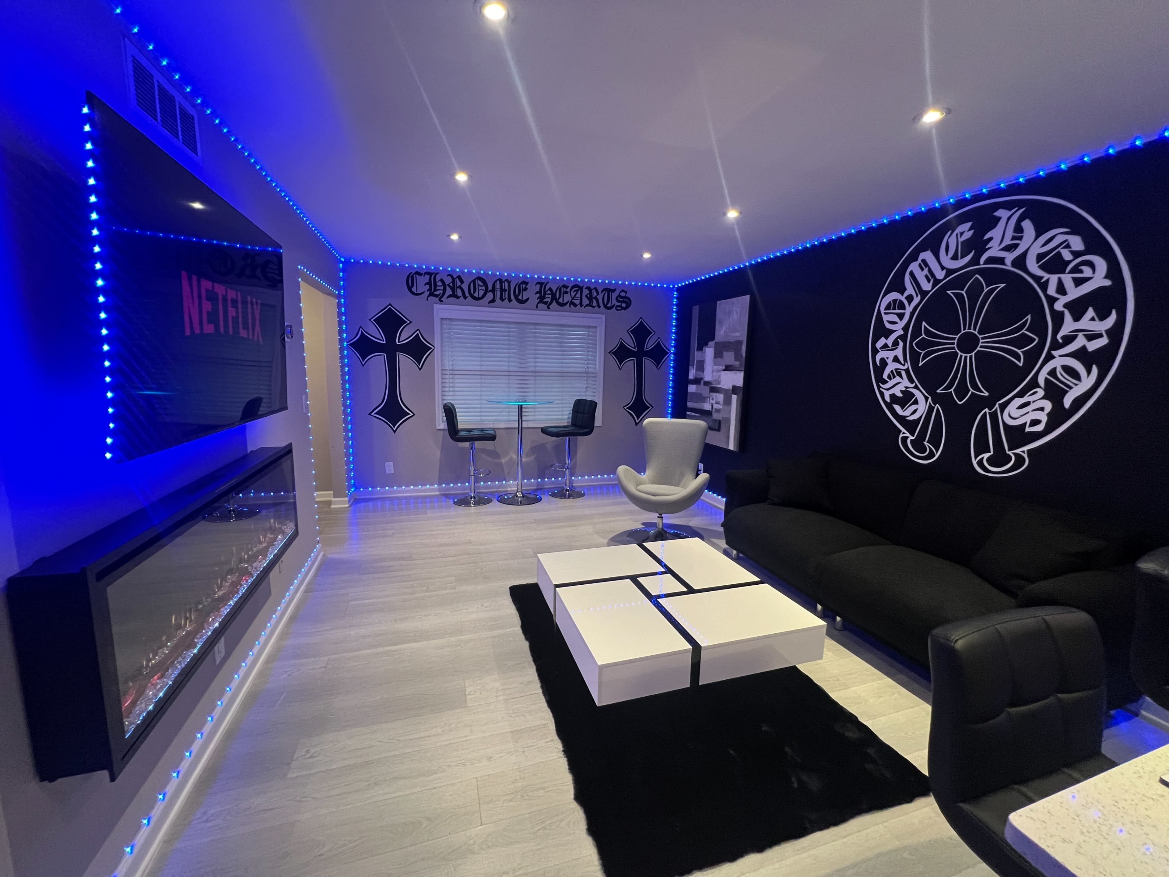 The room features a modern design with black and white furniture, neon blue lighting, and decorative wall art.