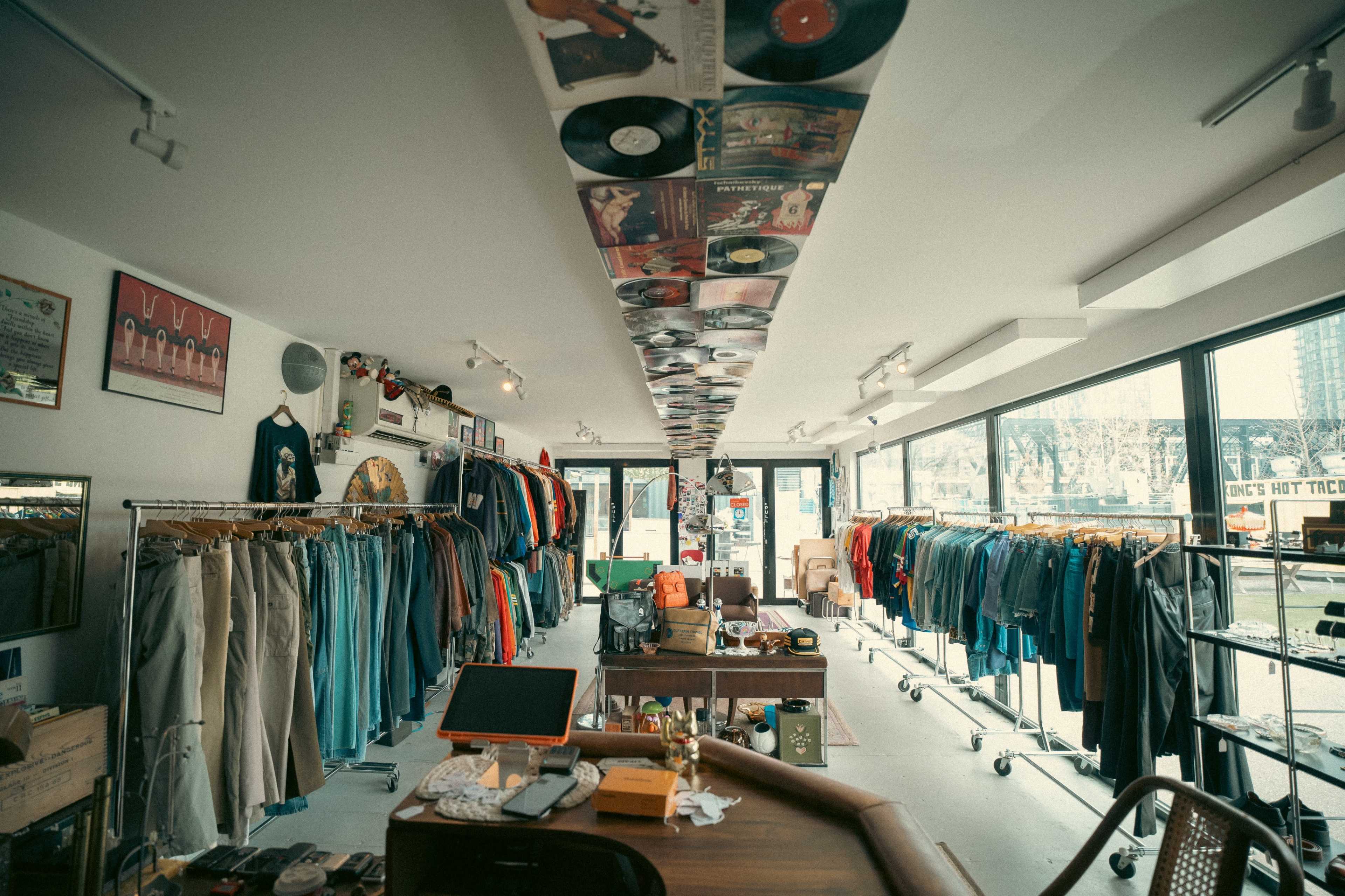 A vintage clothing store features racks of apparel and vinyl records displayed on the ceiling.