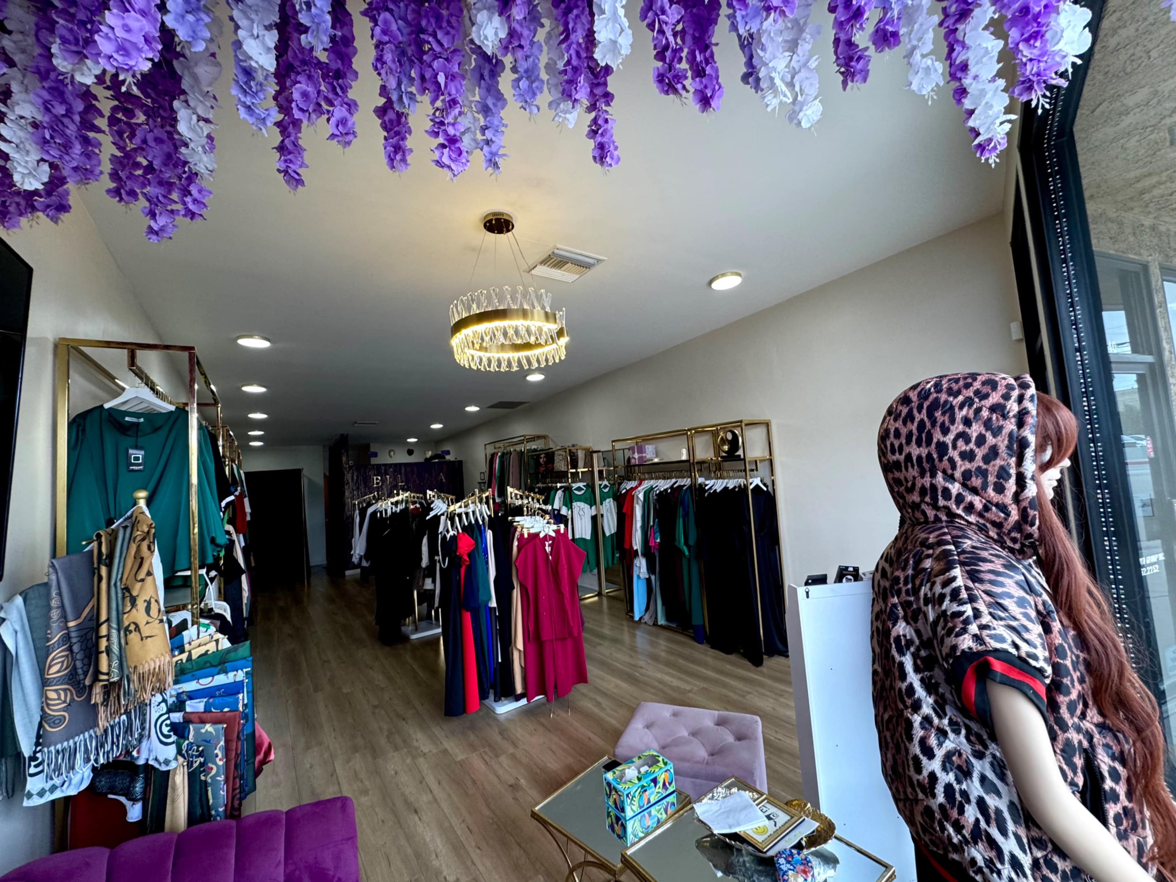 The image shows a boutique interior featuring clothing racks filled with various garments and a mannequin displaying a leopard print outfit near the entrance.