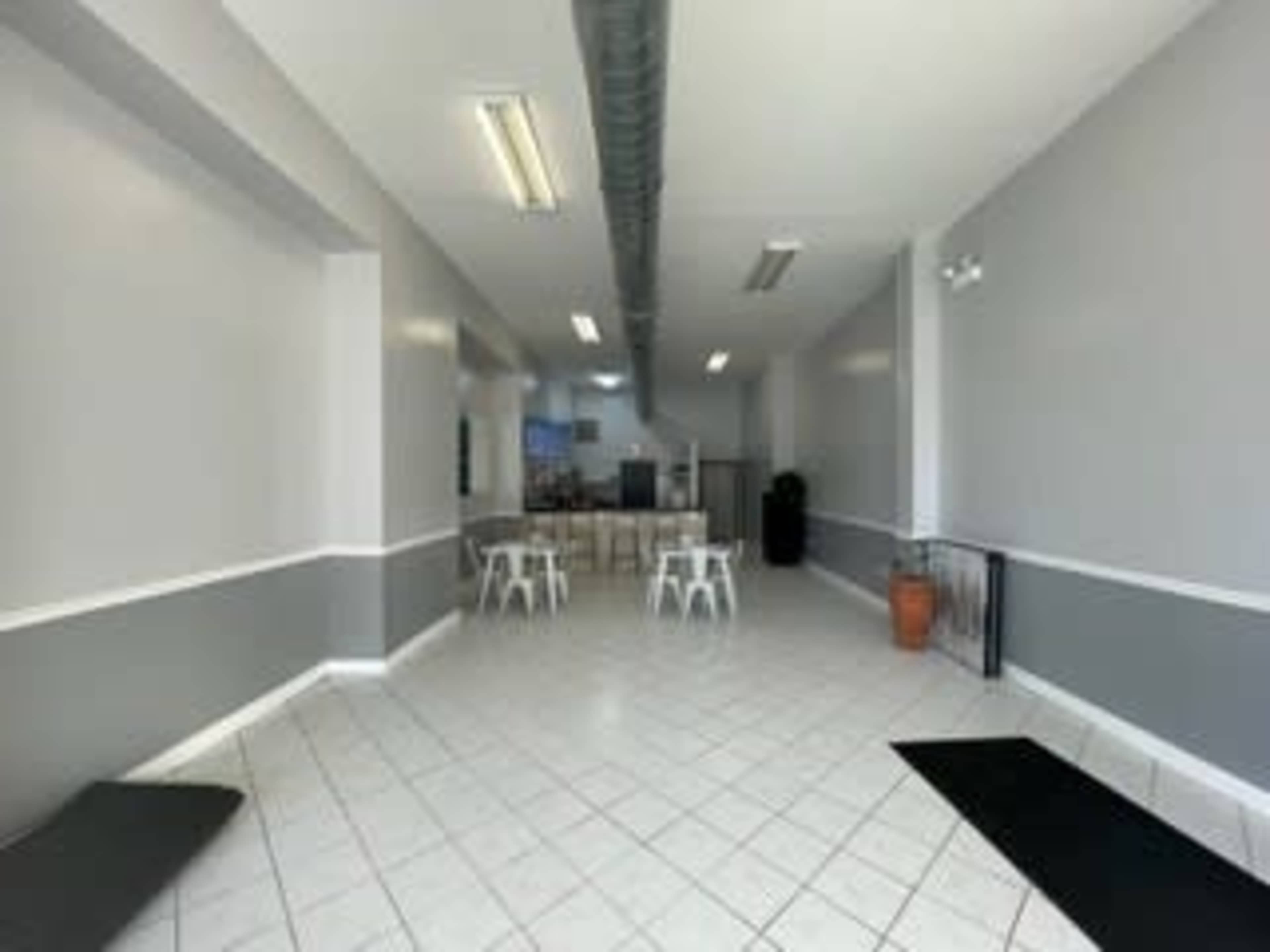 A spacious, empty room with tile flooring, gray walls, and white furniture, featuring several small tables and chairs.