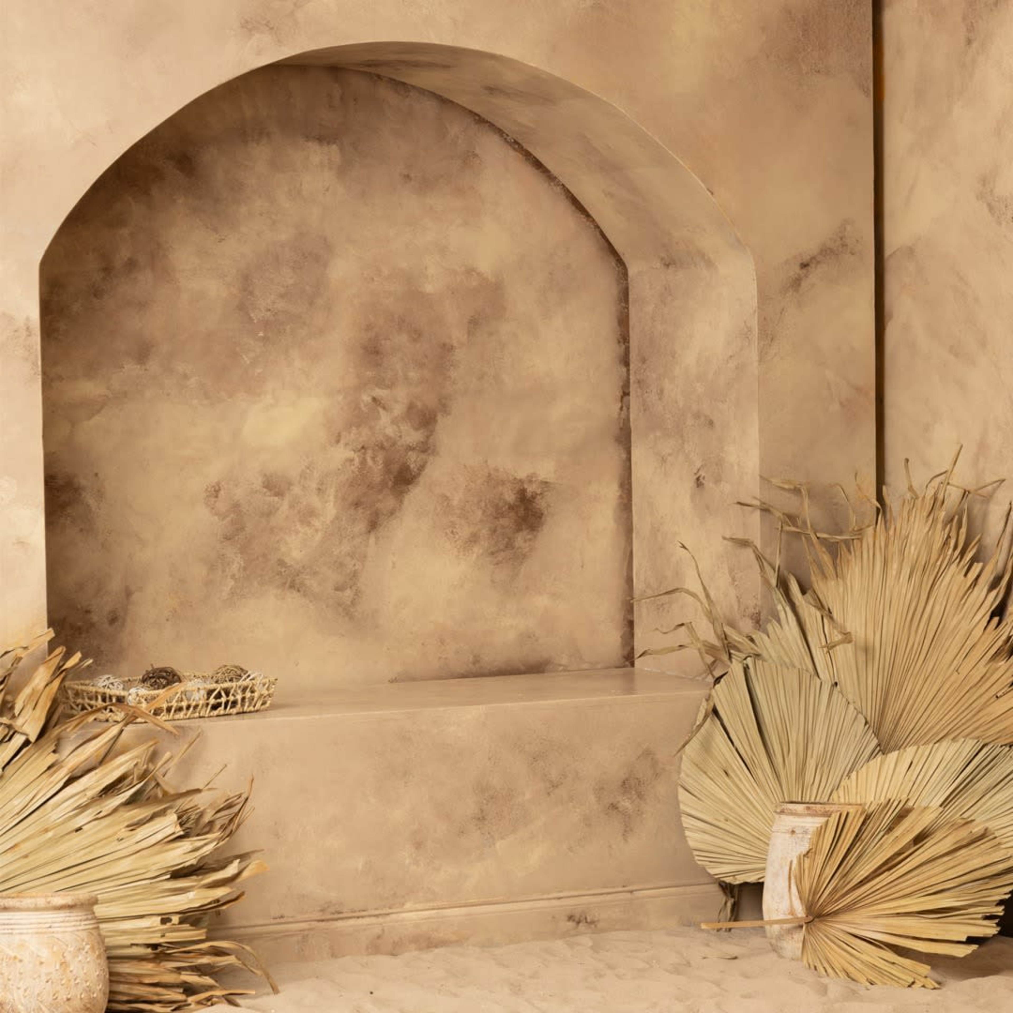 A textured beige wall with a curved indentation and decorative dried palm leaves arranged beside a ceramic vase.
