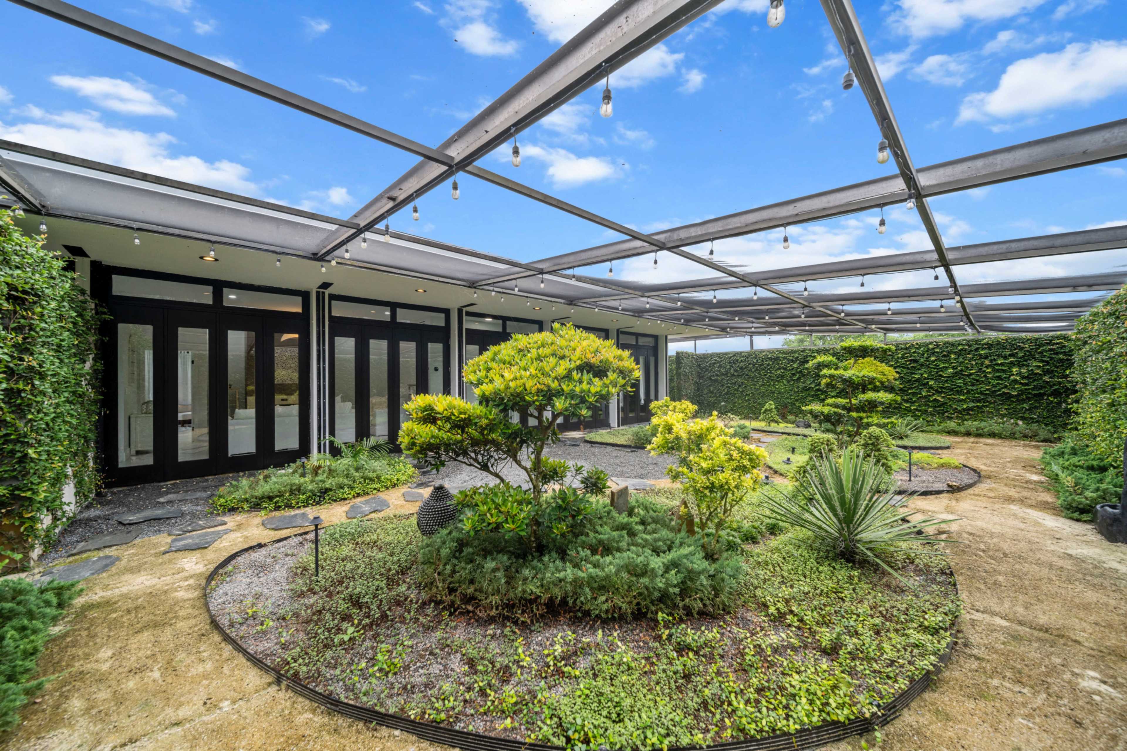 The image shows a garden area surrounded by a glass-covered structure, featuring landscaped greenery and decorative plants.