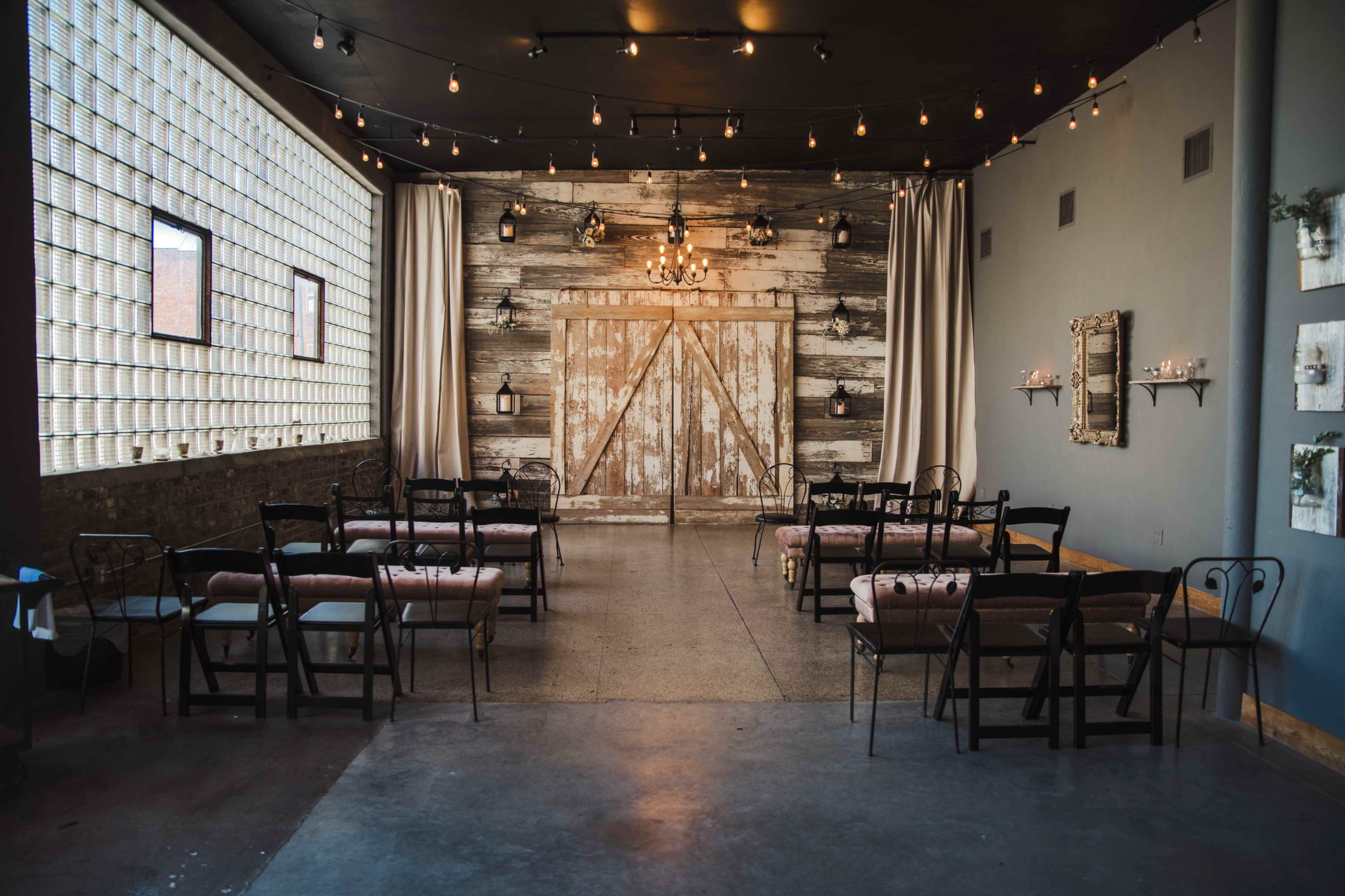 An indoor event space with wooden accents, string lights, and rows of chairs arranged facing a decorative wooden backdrop.