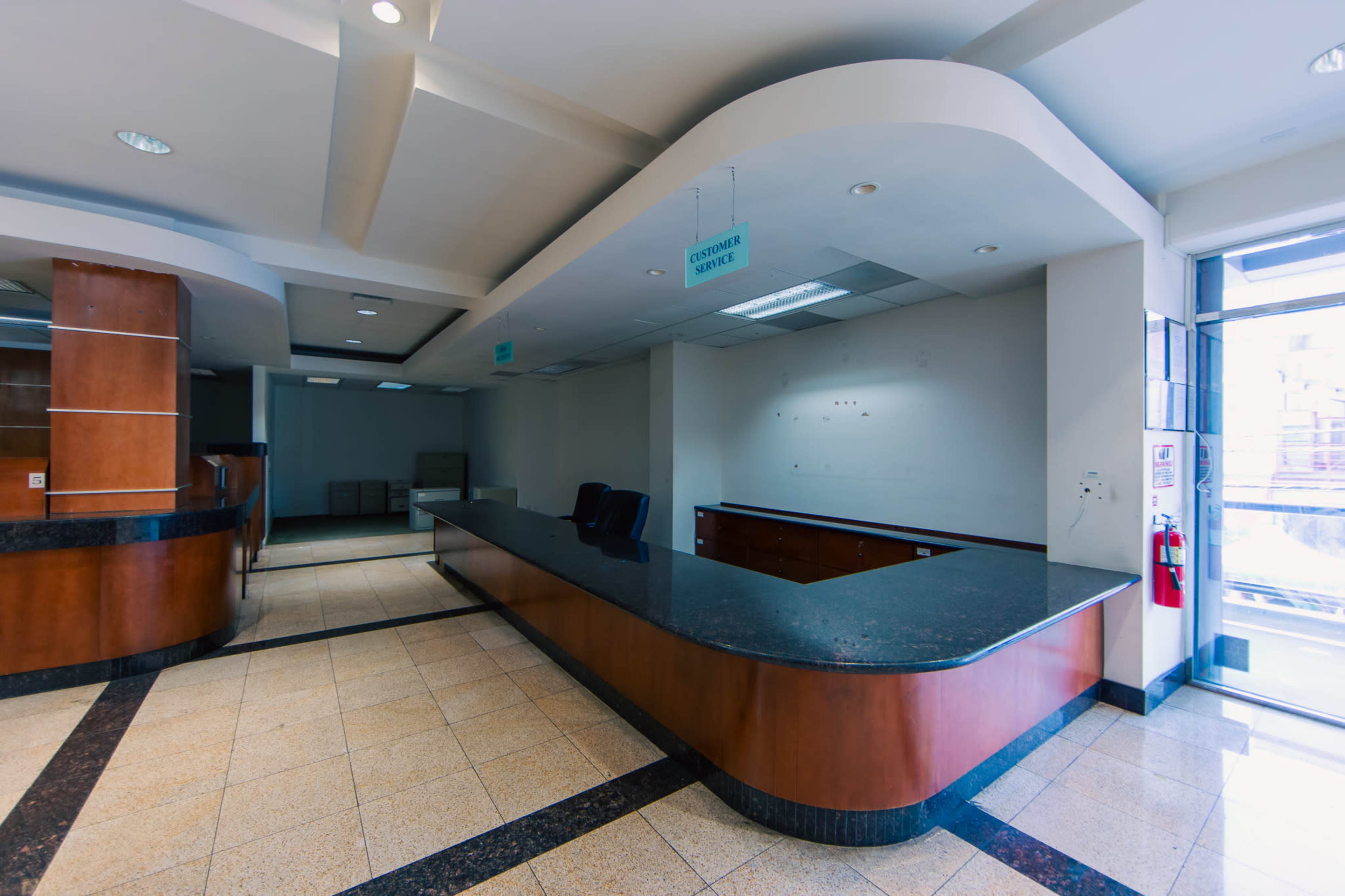 The image shows an empty reception area with a curved counter, wooden paneling, and a large window providing natural light.