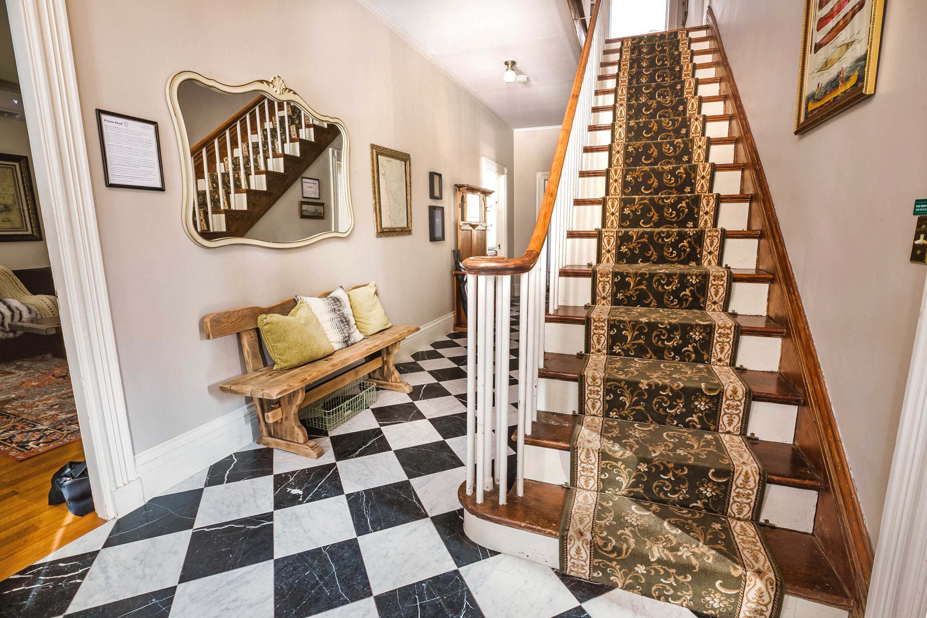 A hallway features a patterned staircase, a checkered floor, and a wooden bench with decorative pillows.