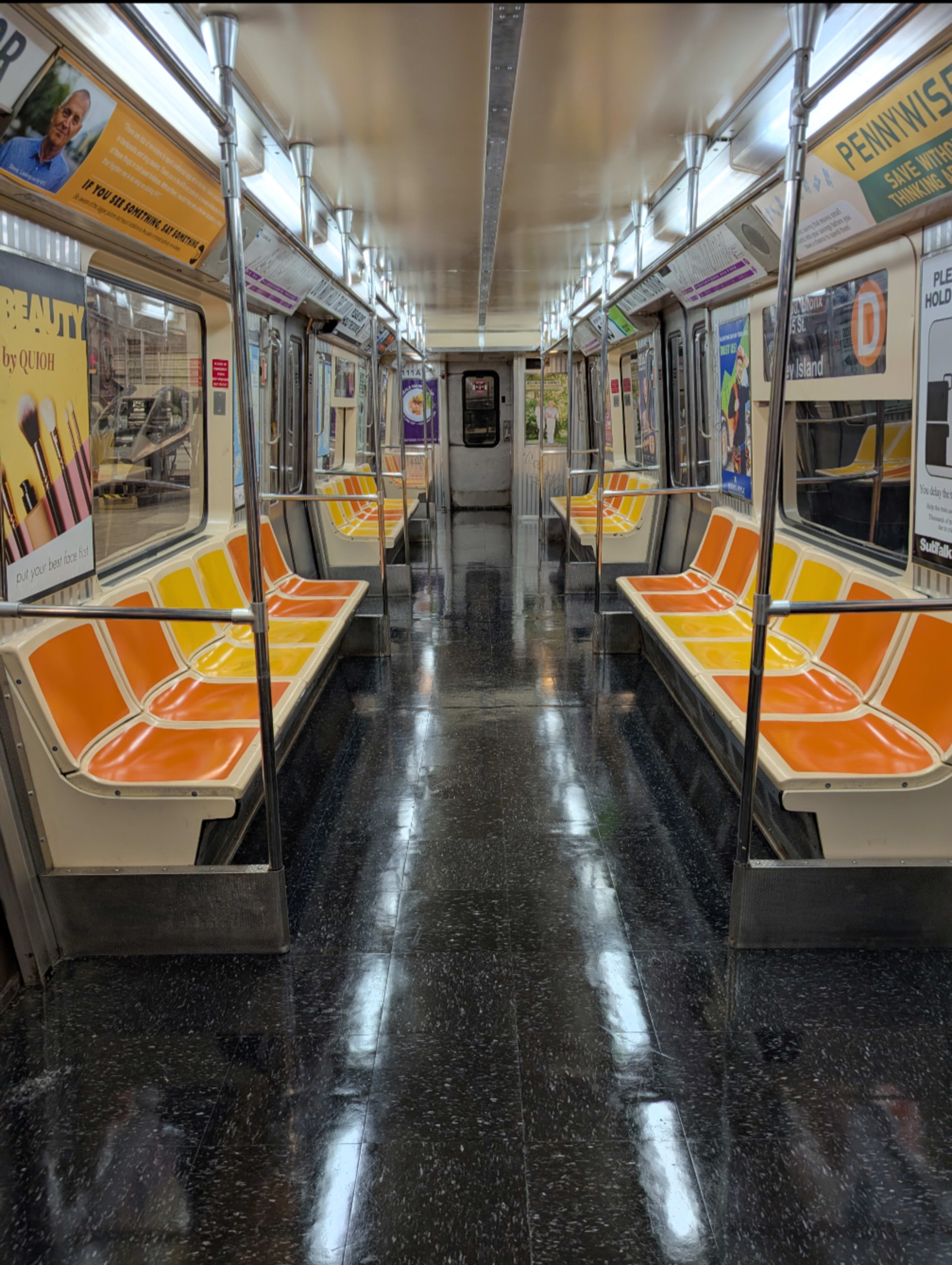 The image shows a vacant subway train interior with orange and gray seats and illuminated overhead lights.
