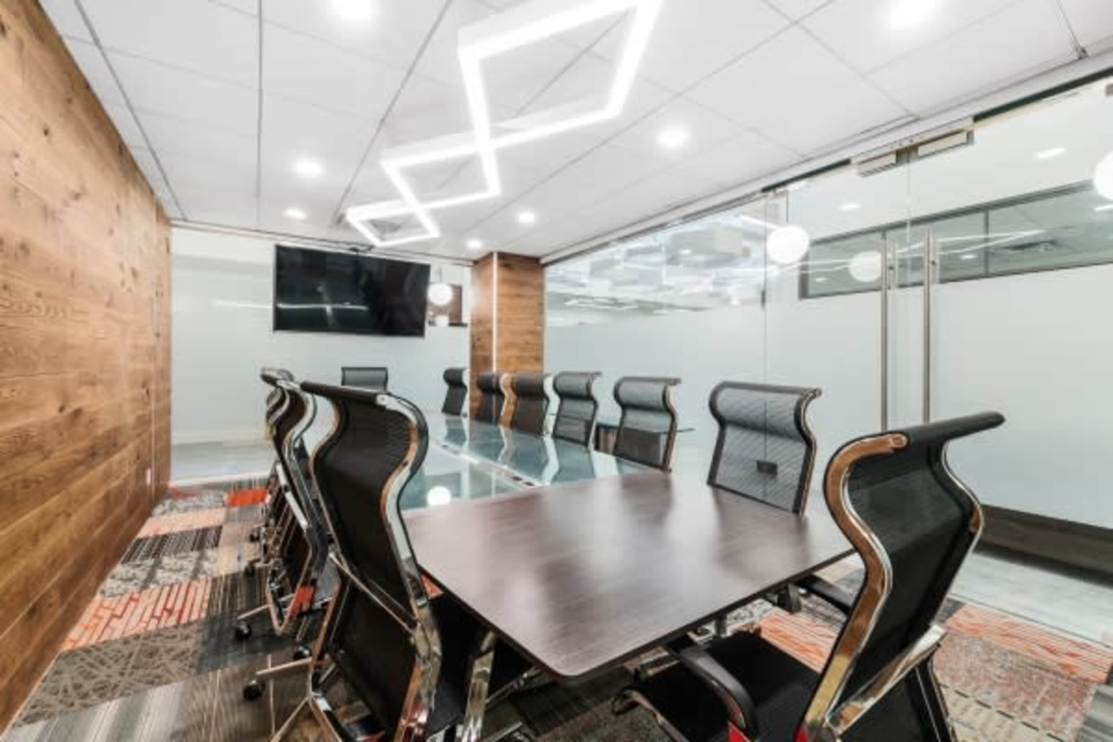 A conference room features a large table surrounded by chairs and a wall-mounted screen.