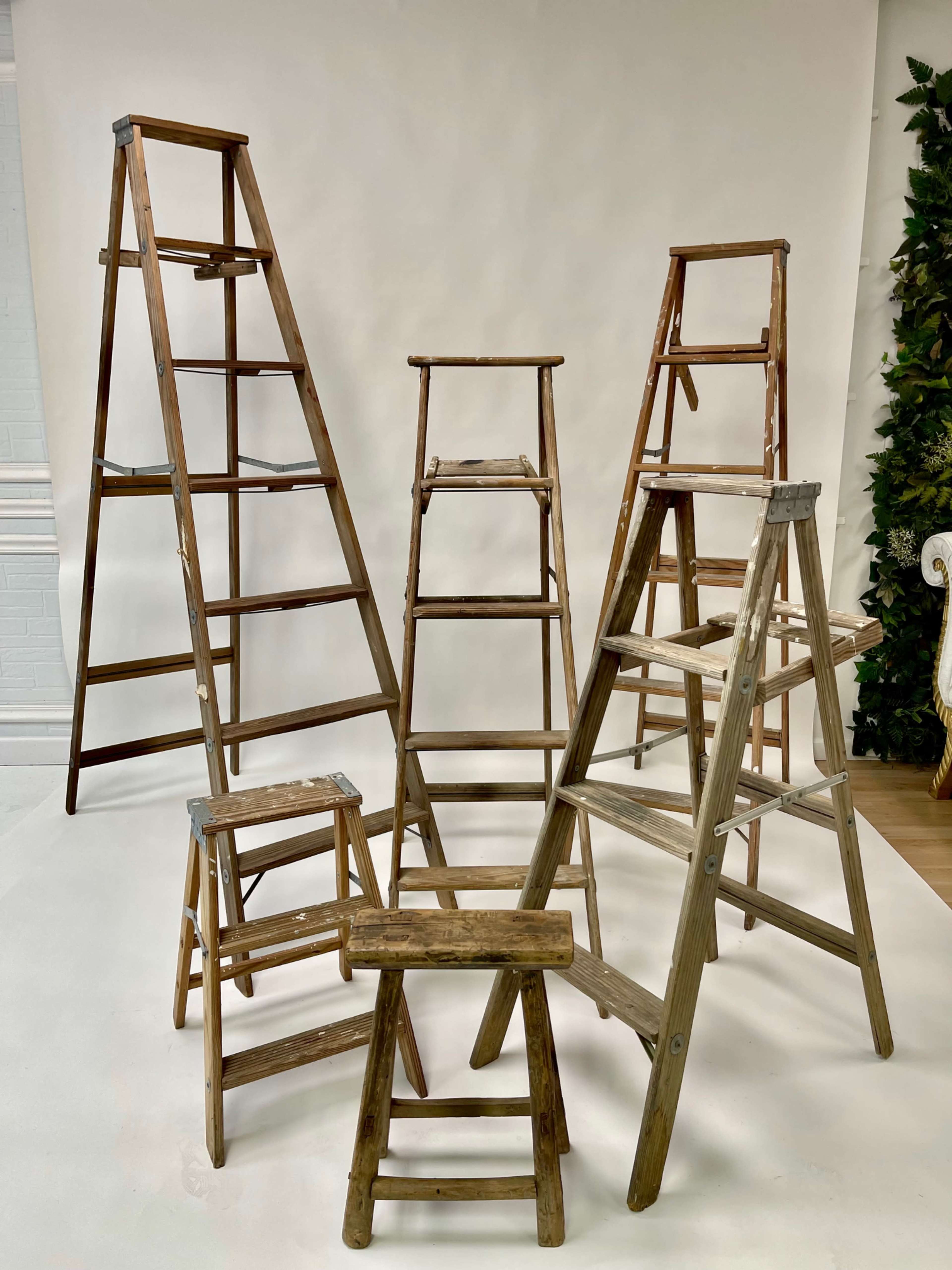 The image shows several wooden ladders arranged in a symmetrical pattern against a plain backdrop.
