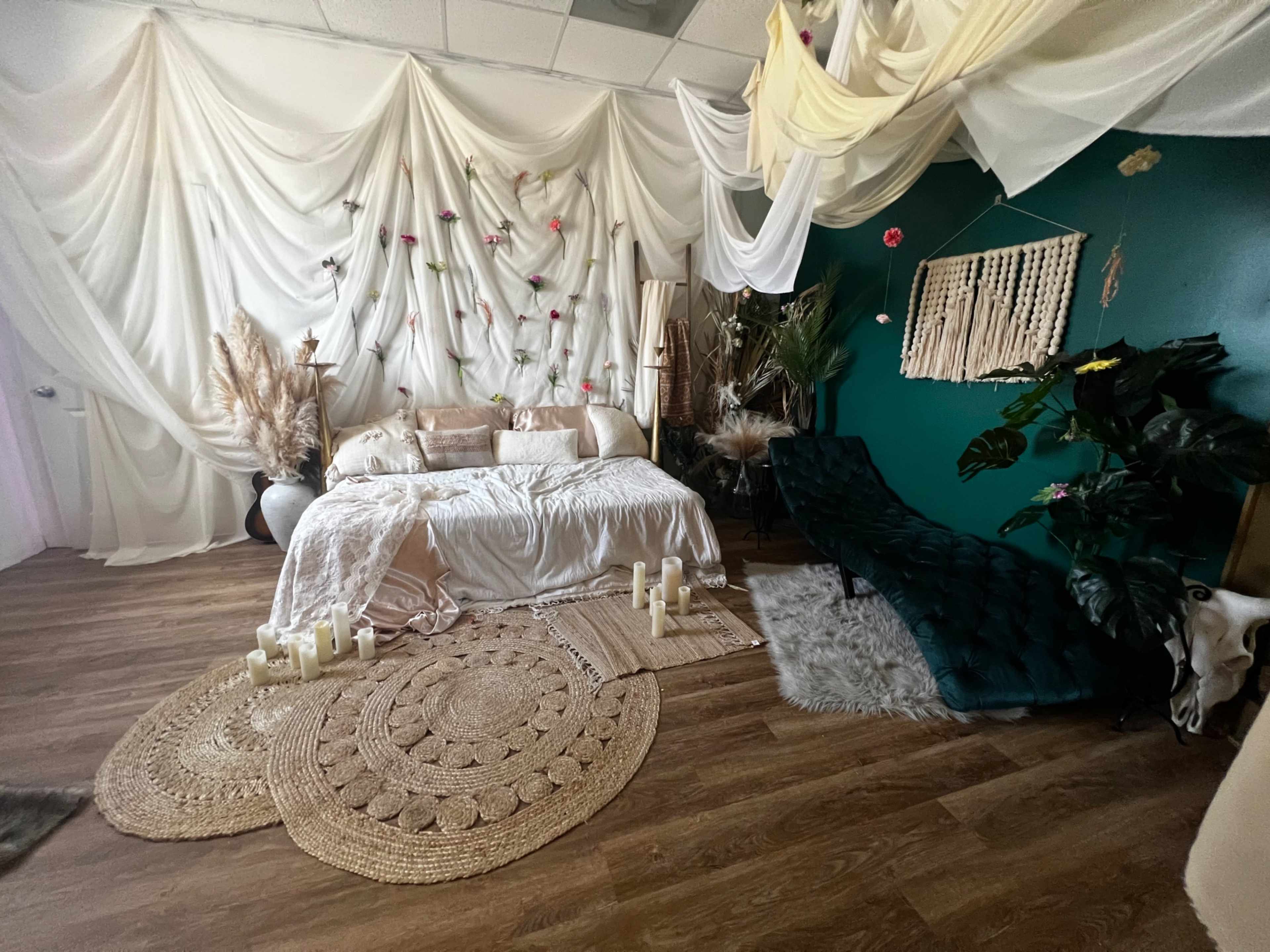 A room decorated with flowing fabric drapes, a light-colored sofa, various plants, and candles arranged on a woven rug.