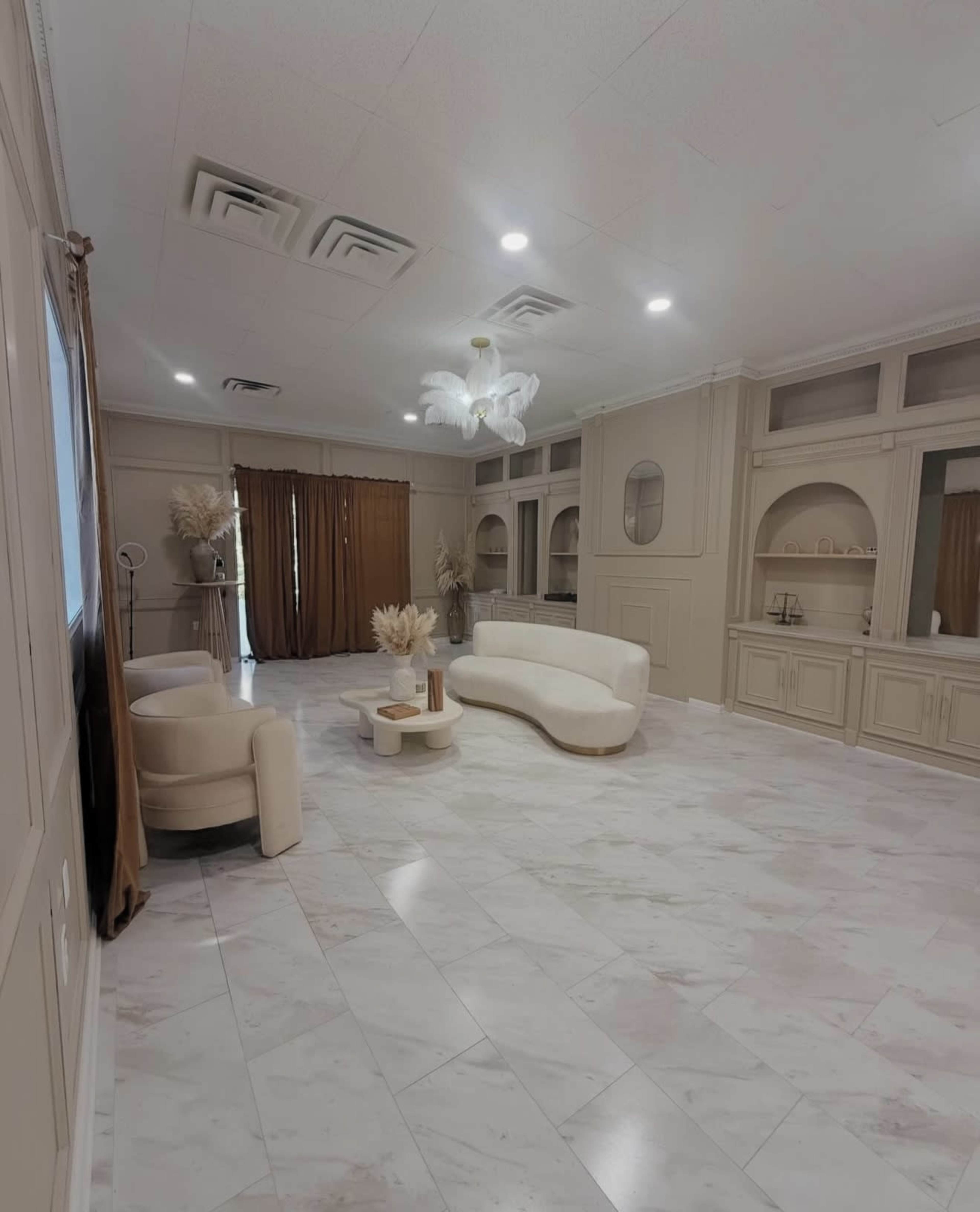 The image shows a spacious, elegantly furnished room with marble flooring, a curved white sofa, a round coffee table, and decorative elements on a light-colored wall.