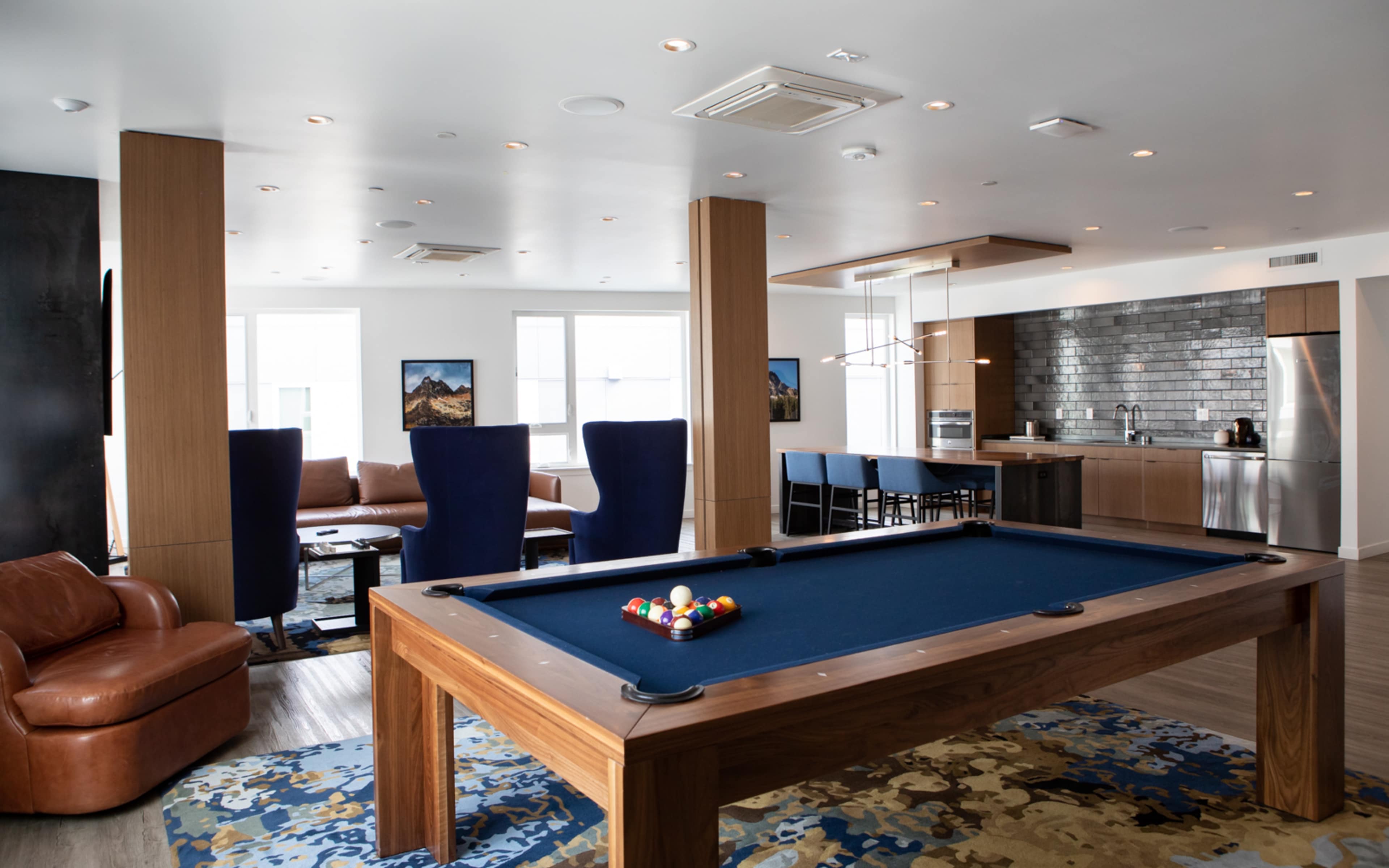 A modern recreational room with a pool table in the center, adjacent to a kitchen and seating area.