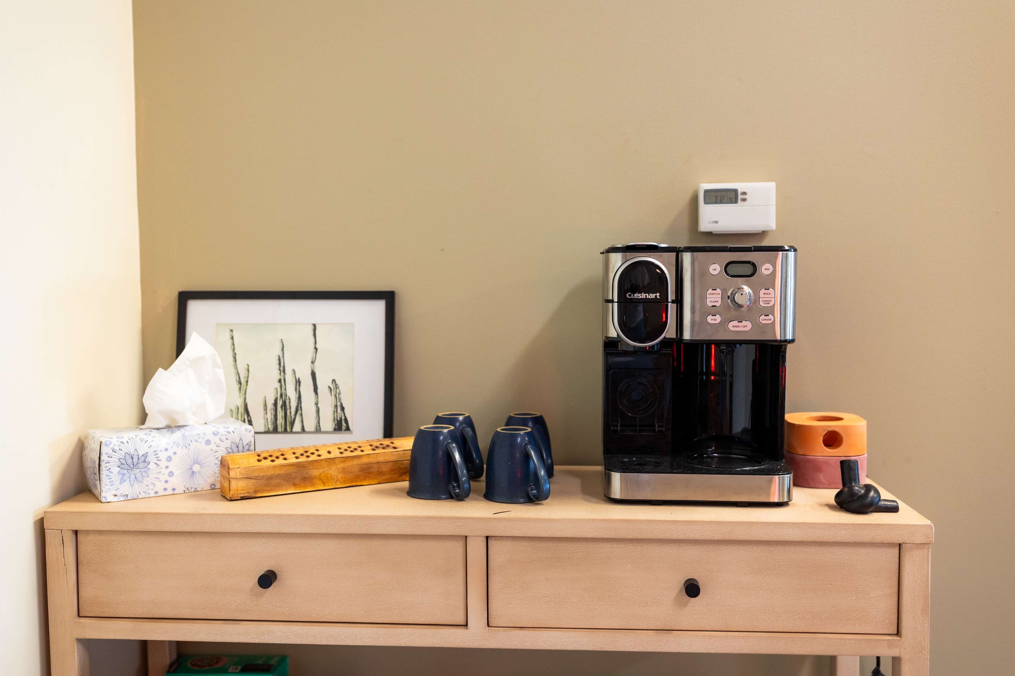 A coffee maker is positioned on a console table alongside cups, a tissue box, and a decorative item.