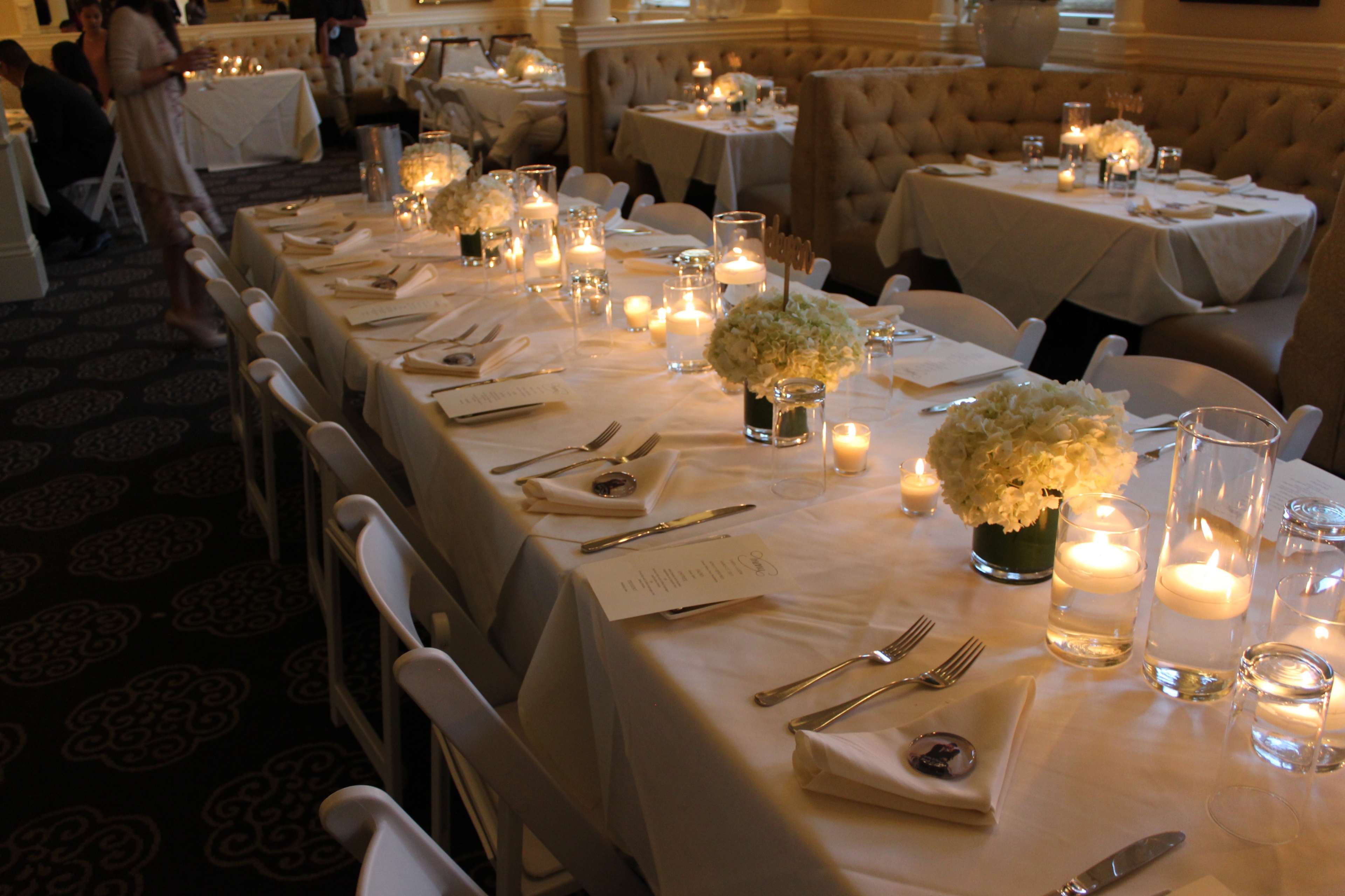A dining setup with elegantly arranged tables featuring white tablecloths, floral centerpieces, and candles.